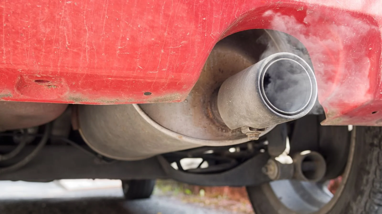 Close-up of car exhaust pipe on underside of a red vehicle with part of the rear wheel visible.