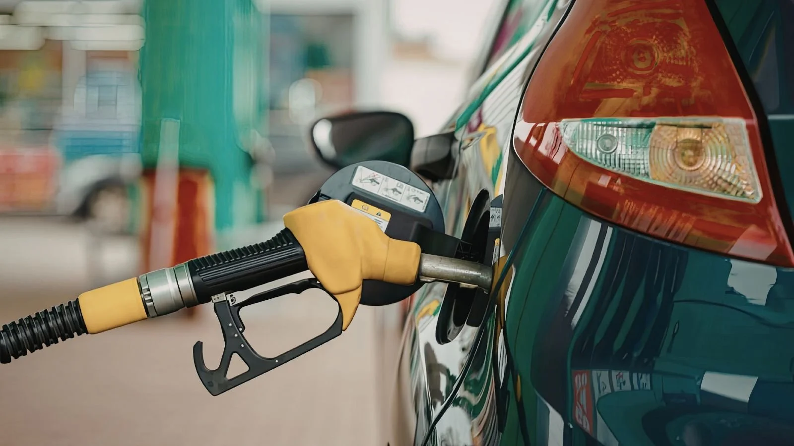 A fuel nozzle inserted into the fuel tank of a green vehicle at a gas station.