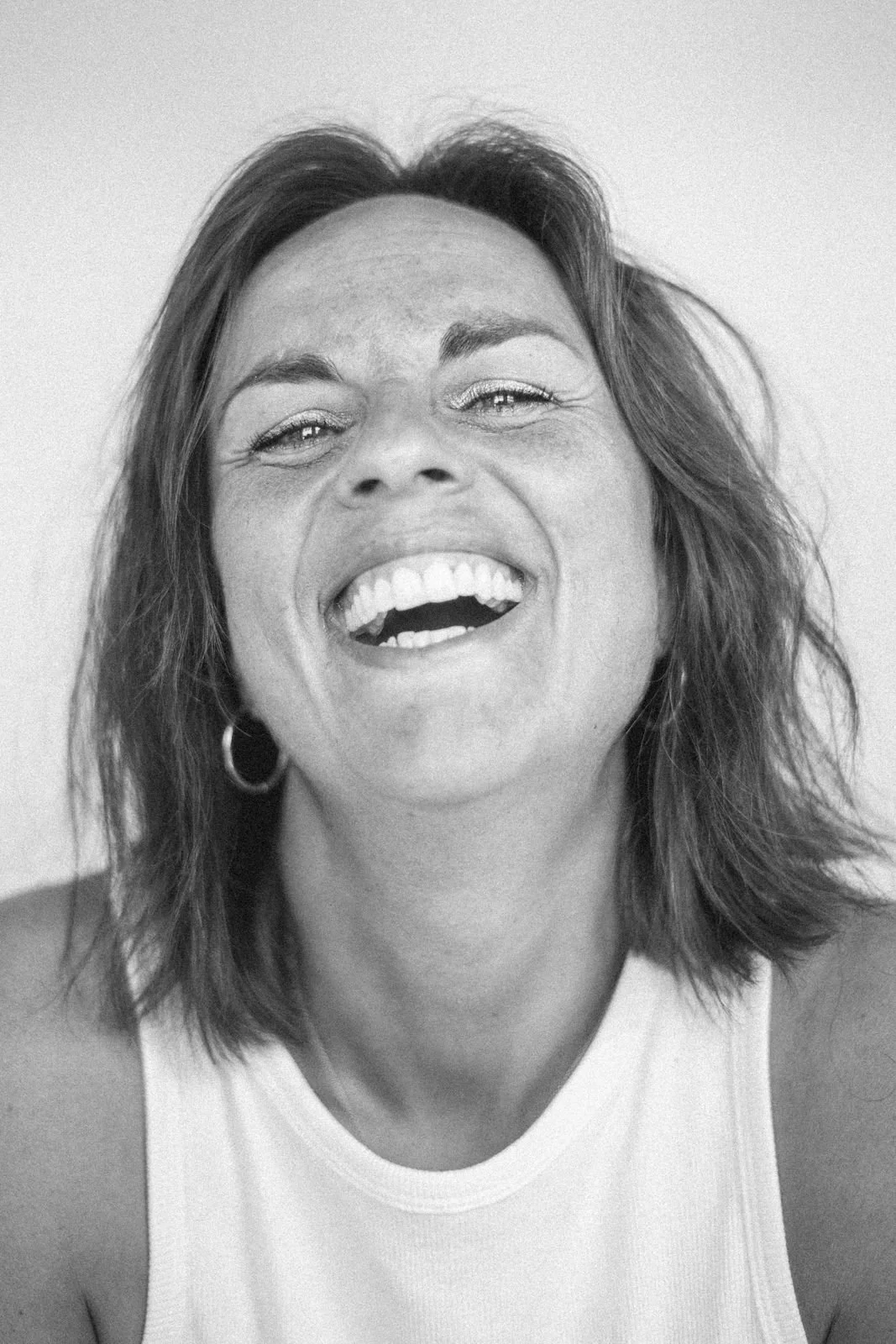 Lächelnde Frau mit kurzen Haaren, in schwarzer und weißer Fotografie, trägt ein weißes Top, trägt Ohrringe.