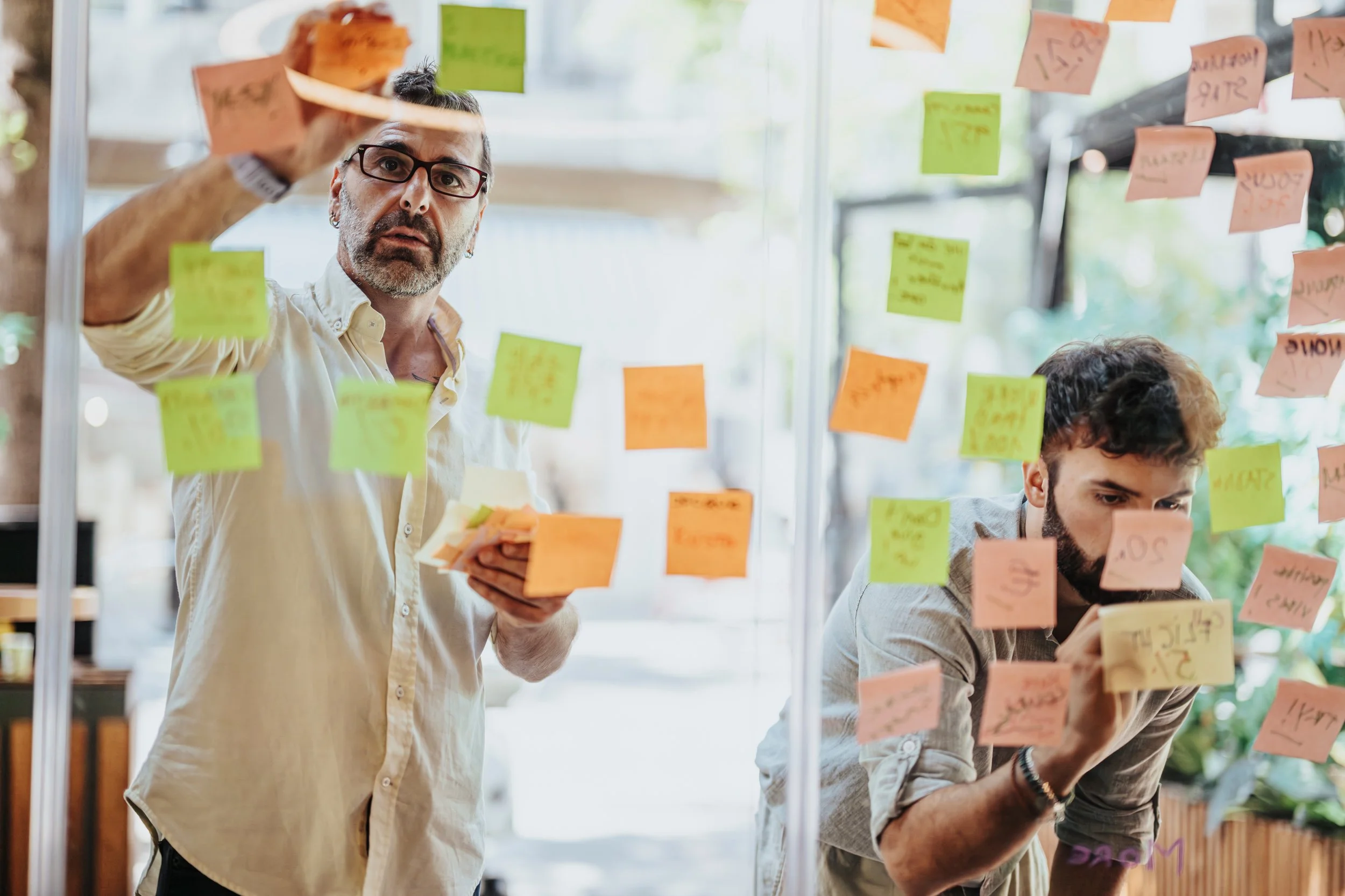 GrowthGenius workshop featuring two business professionals collaborating and organizing sticky notes, representing the transition to a synchronized revenue engine with predictable, not exhausting, growth and veteran leadership