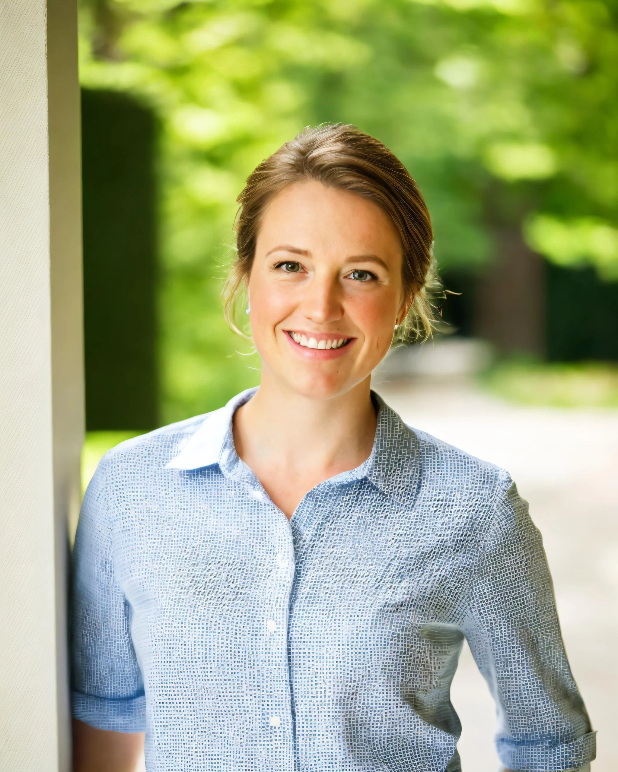 Smiling woman in blue shirt outdoors with blurred green background