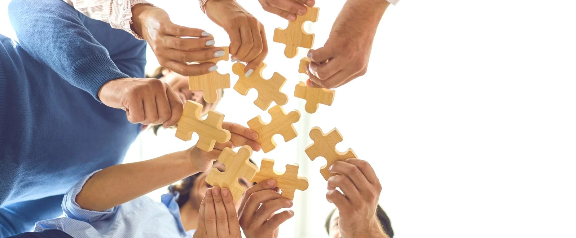 Multiple hands connecting wooden puzzle pieces, representing the GrowthGenius modular approach to identifying and solving critical bottlenecks in a commercial engine for immediate quick wins