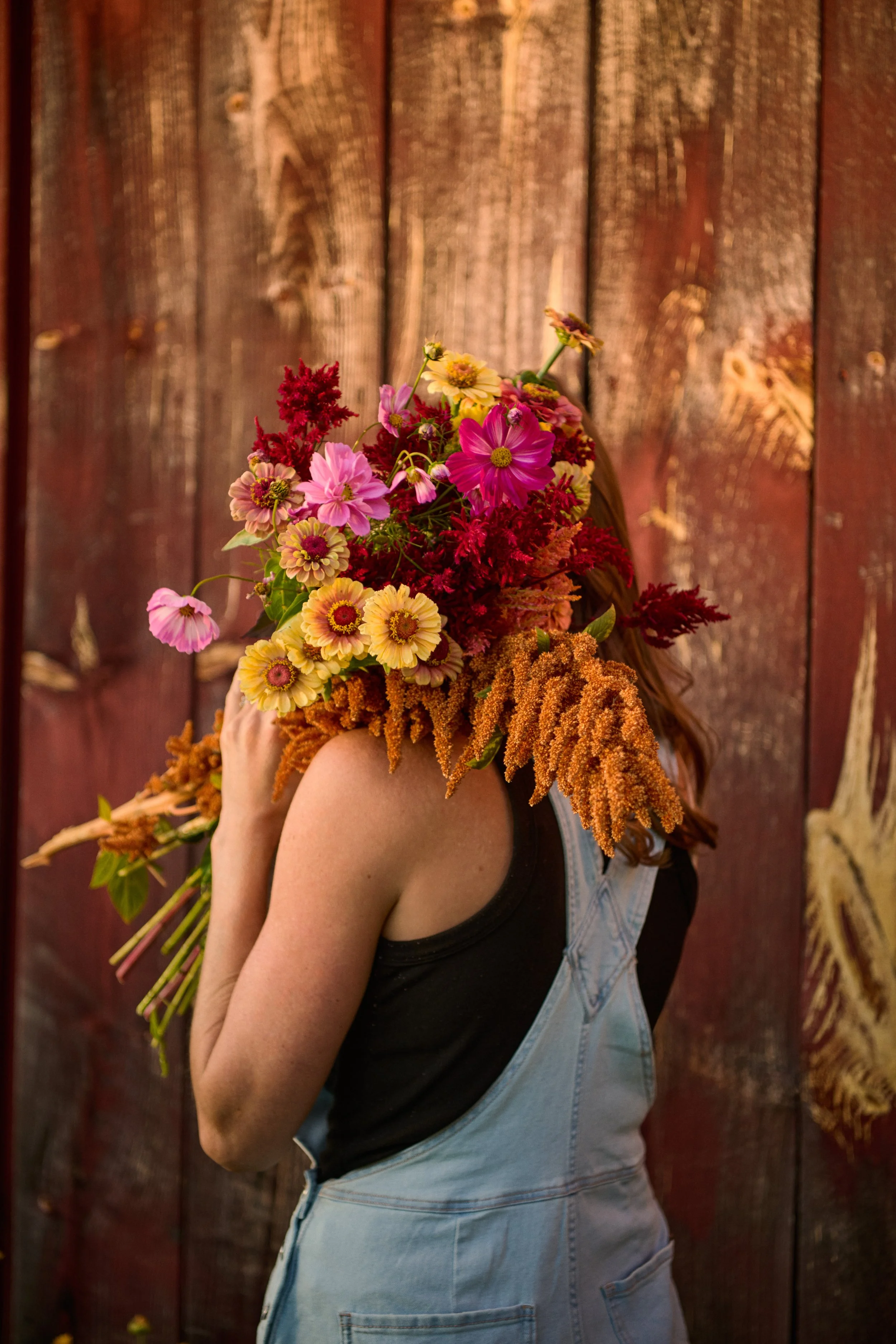 Person holding a bouquet of colorful flowers, standing against a wooden background.