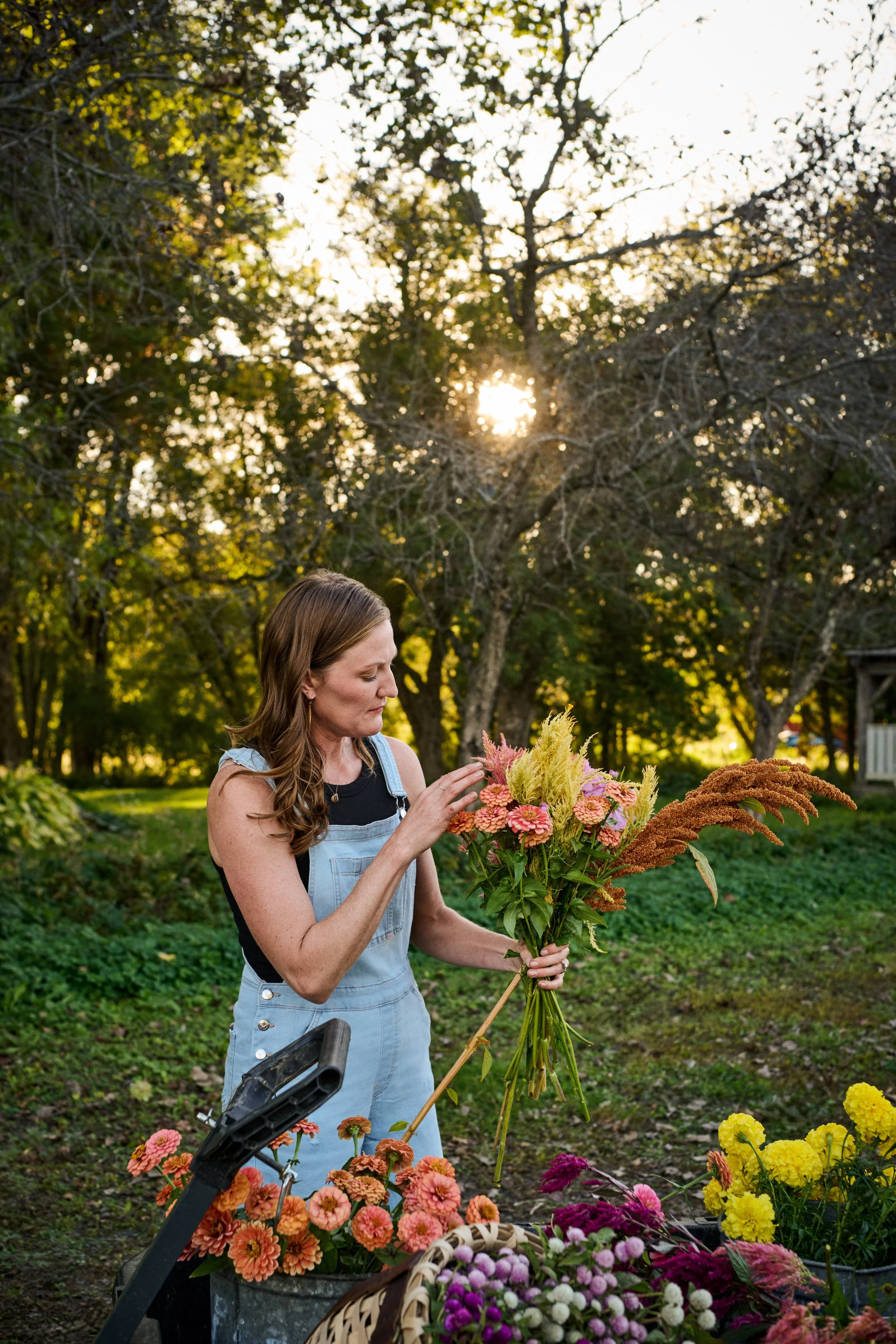 Woman arranging a bouquet of flowers outdoors, with a sunny background and trees.