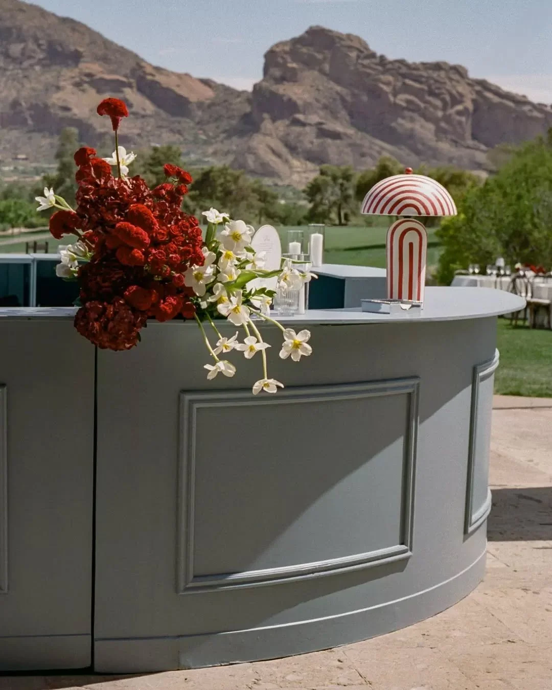 The custom paint color on our Signature Oval Bar is called "Rainy Season." This cocktail hour at @paradisevalleycountryclub was anything but. ☀️

Deep red florals by @mintgreendesign against that cool grey-blue finish - bold call, perfect p