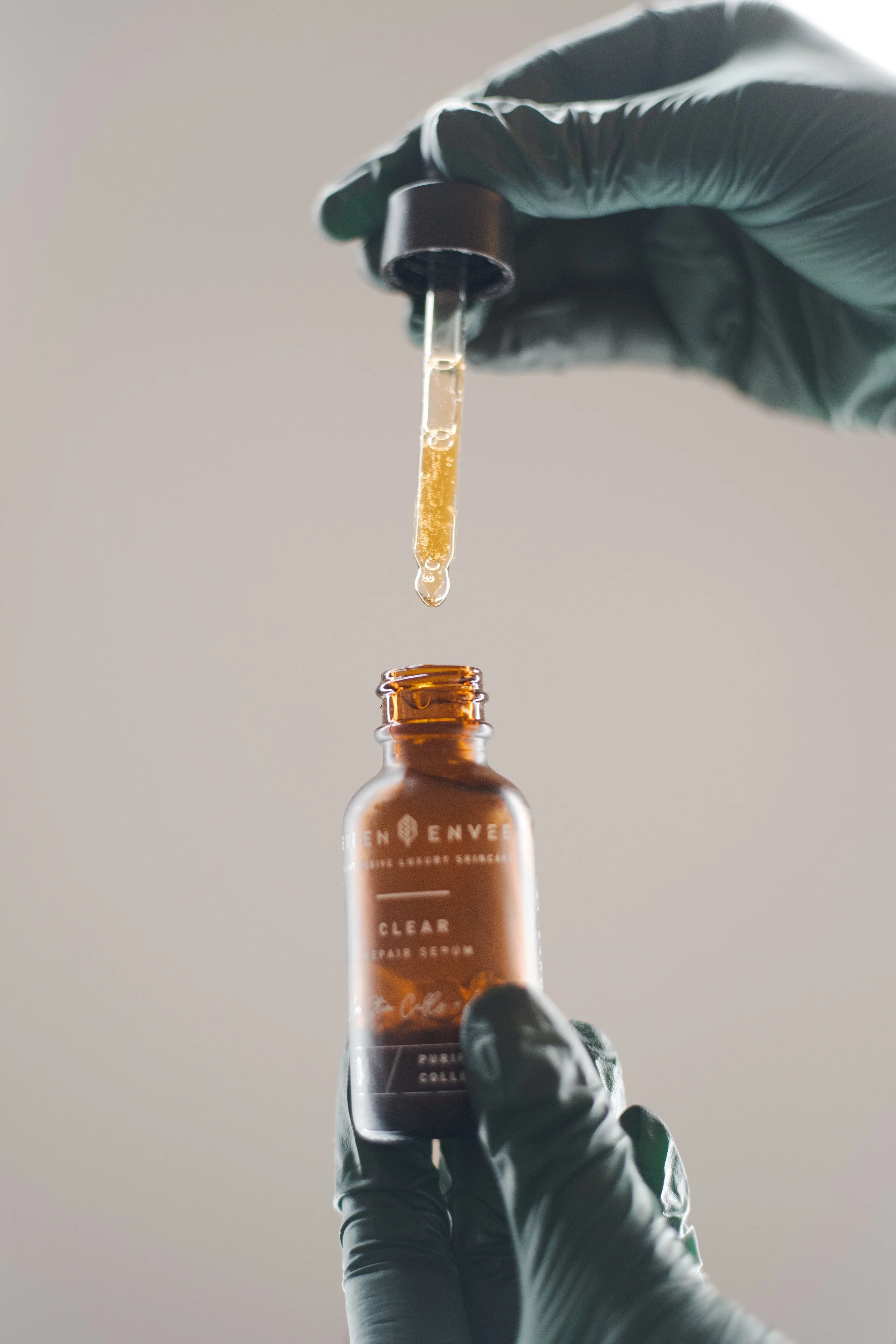 Gloved hands holding a bottle of Green Envee serum and the dropper full of product