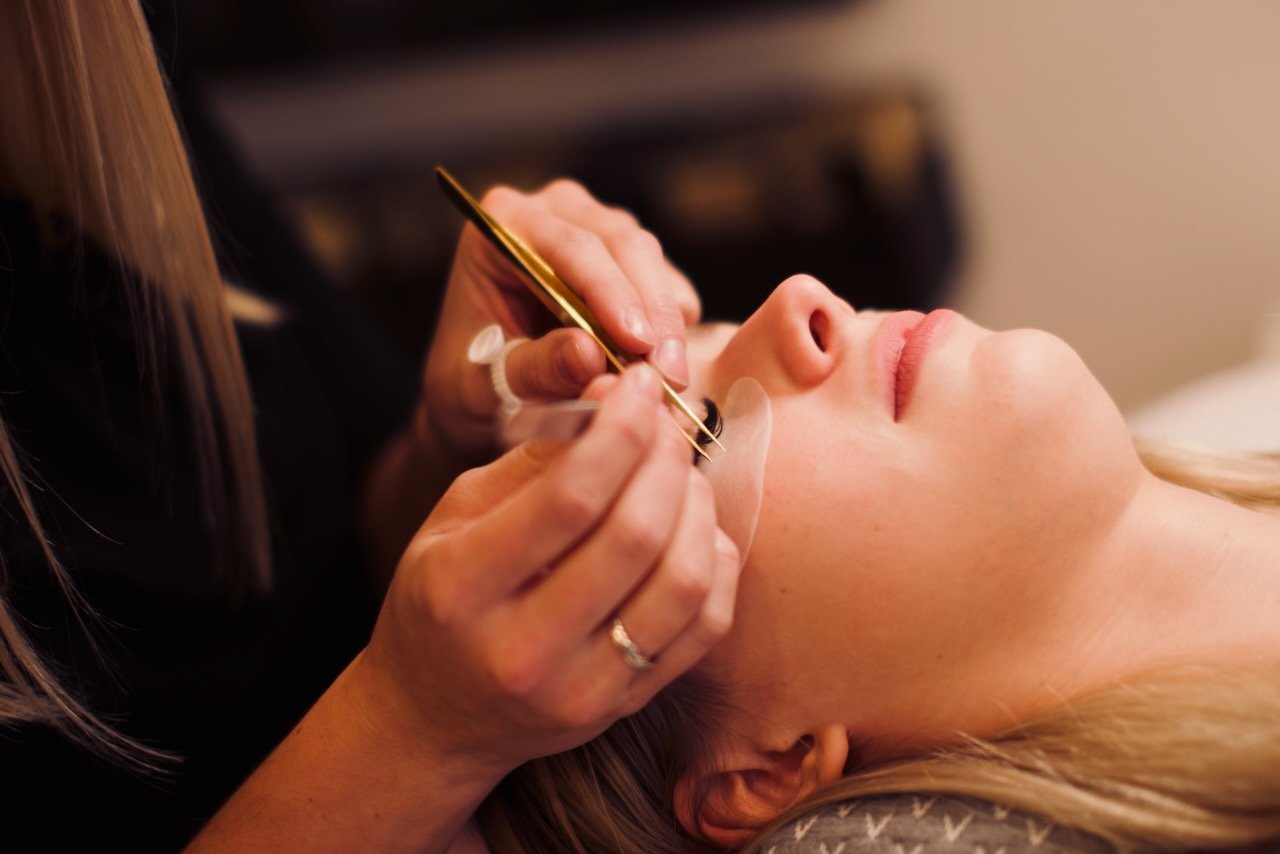A person getting eyelash extensions as they lay on a table. The technician applies lashes with tweezers.