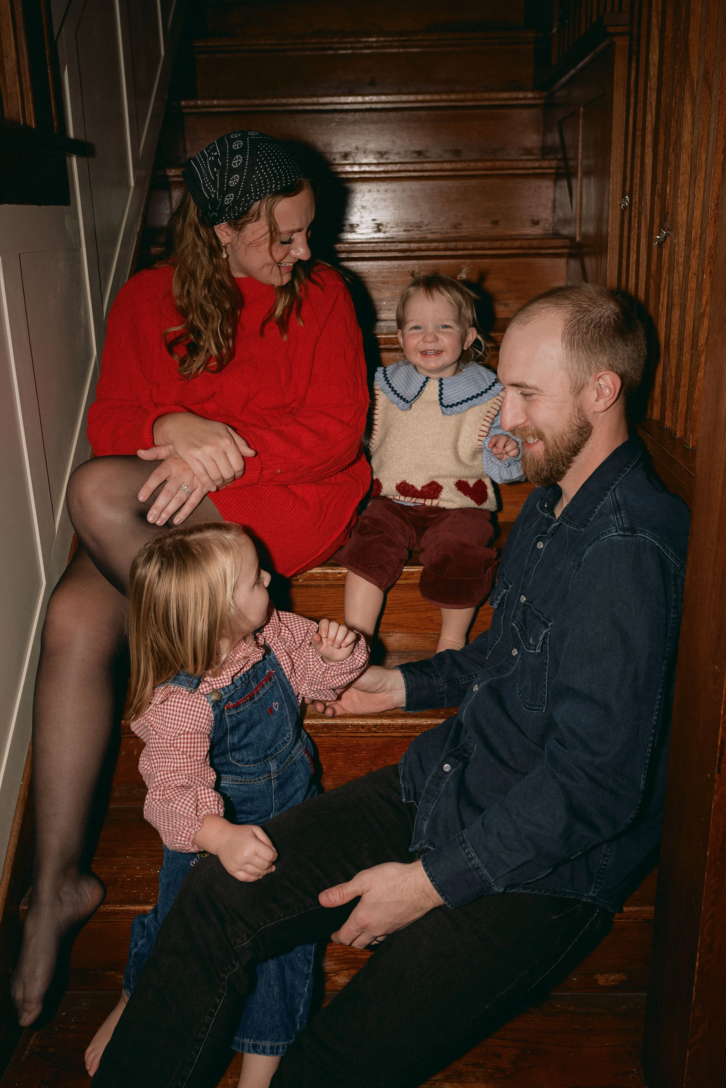 Family playing on a blanket in their backyard, with a man holding a baby, and a woman lifting a child playfully in front of a house.