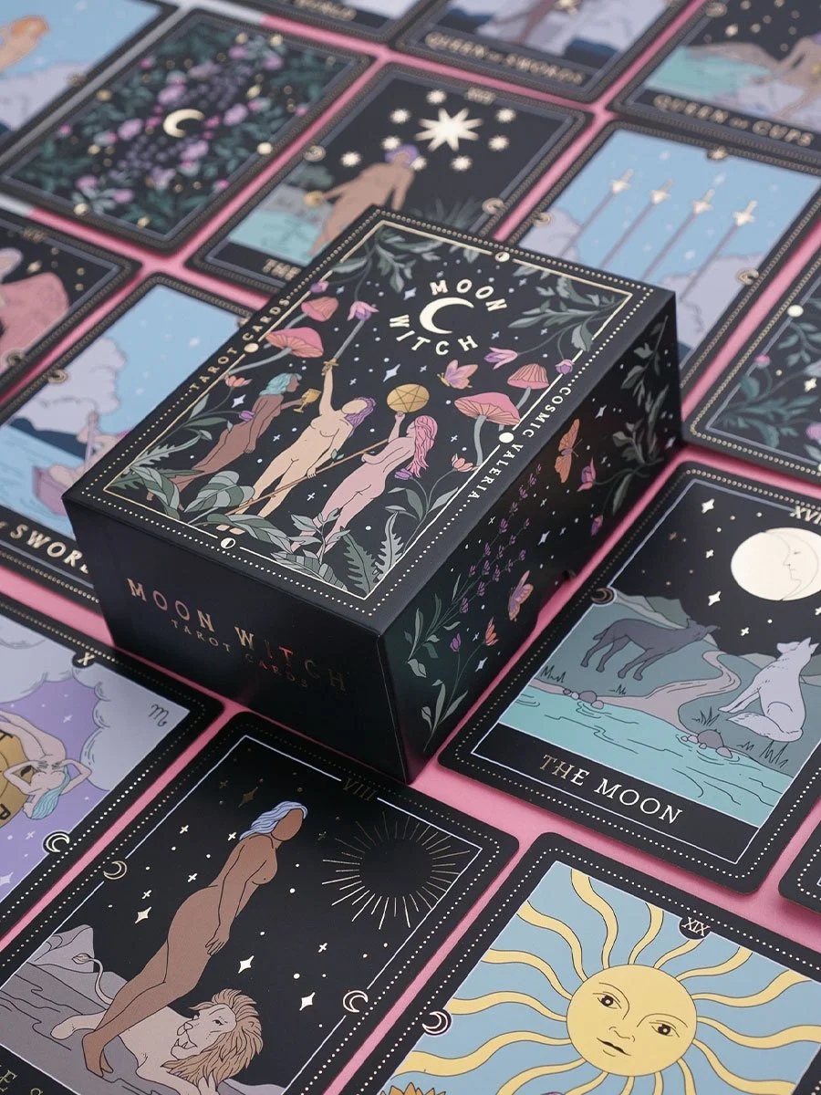 Flat lay of the Moon Witch Tarot Deck by Cosmic Valeria, featuring the deck box and several hand-drawn tarot cards with mystical illustrations of celestial beings, animals, and symbols, including The Moon card.
