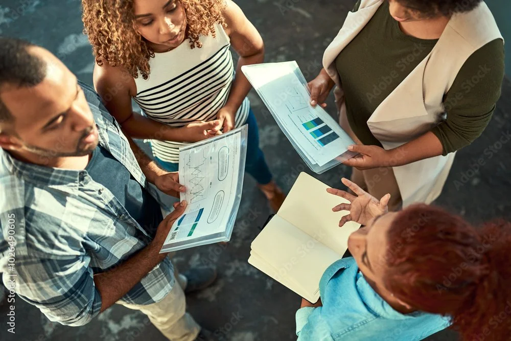 Four people engaged in a business meeting looking at charts and graphs on paper and a notebook.
