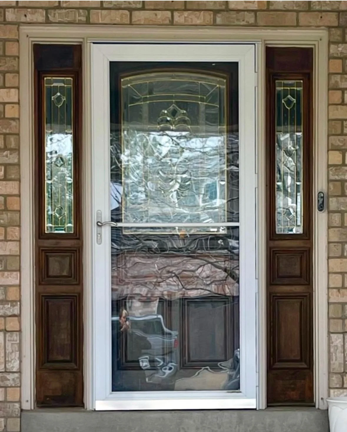 Before: worn wood entry door with leaded glass sidelites behind an aluminum storm door on a Denver-area brick home