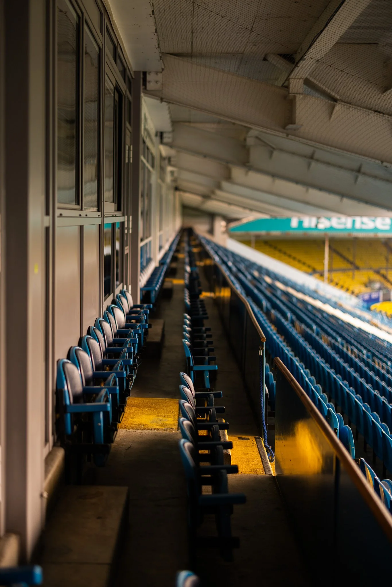 Empty blue stadium seats with sunlight shining on them, viewed from the side aisle.