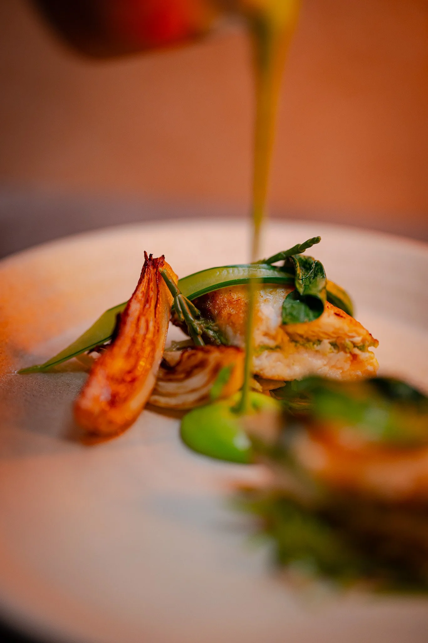 Close-up of a gourmet dish with seared seafood, garnished with green herbs and sauce, being prepared and plated.