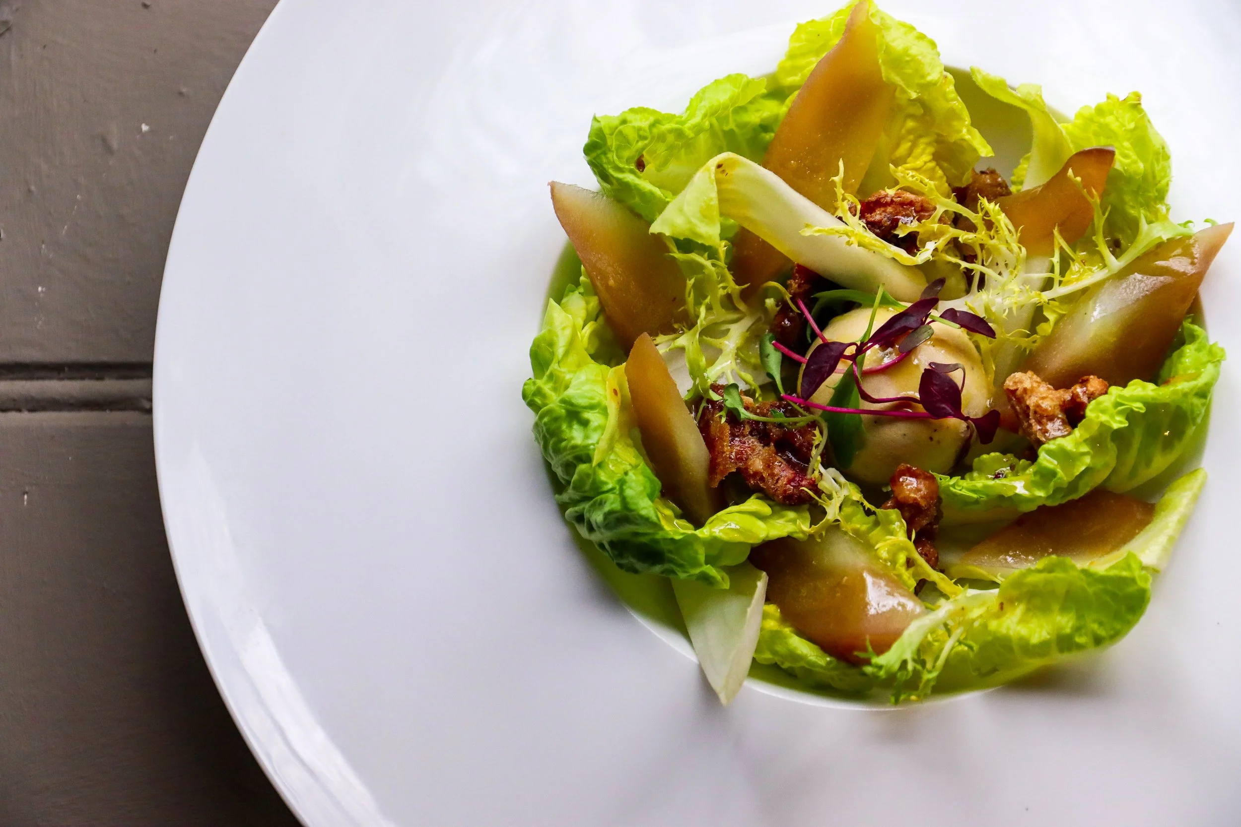 A salad on a white plate with lettuce, pear slices, microgreens, and possibly bacon bits.