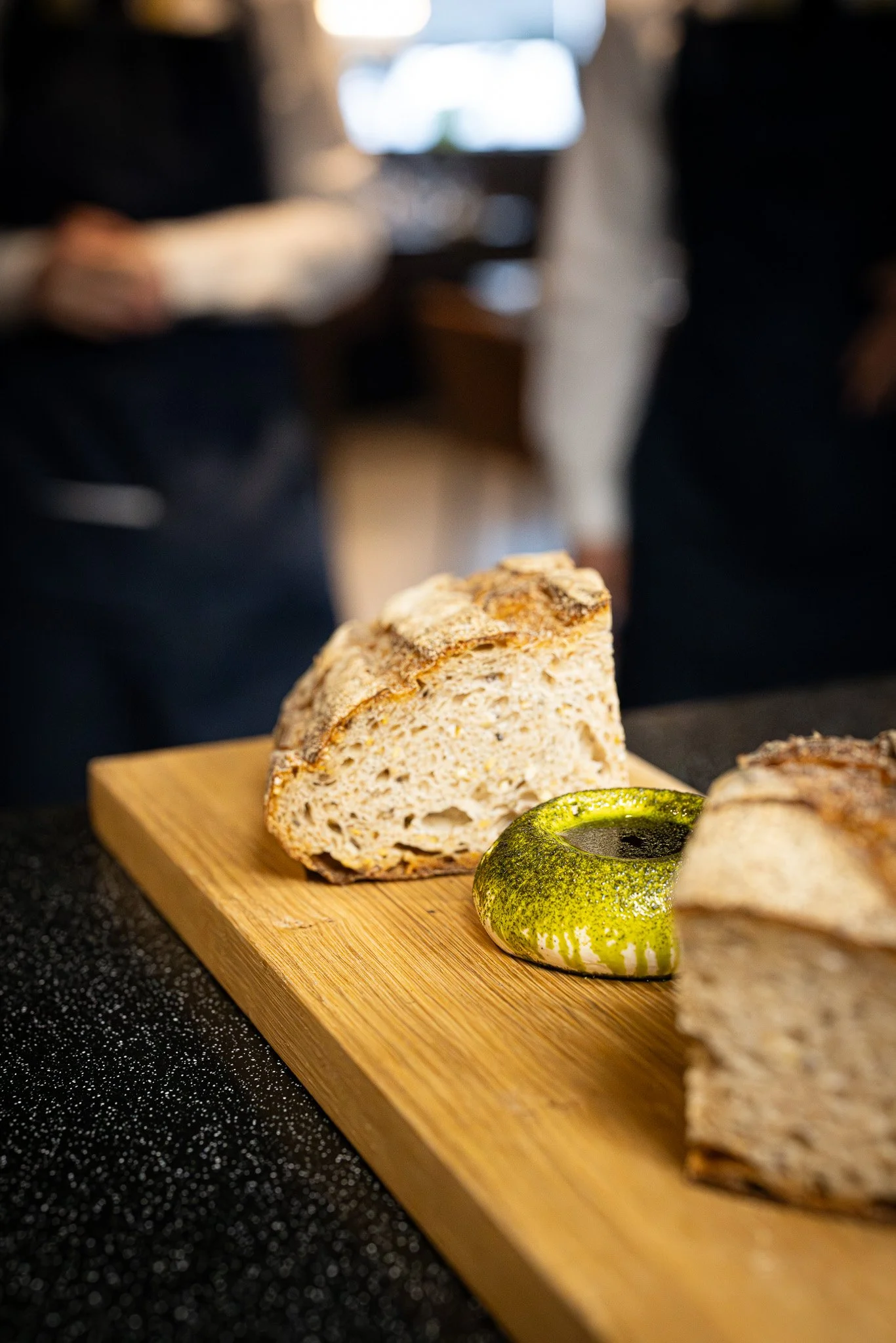 Slices of rustic bread on a wooden cutting board with a green ceramic cup nearby in a kitchen setting.