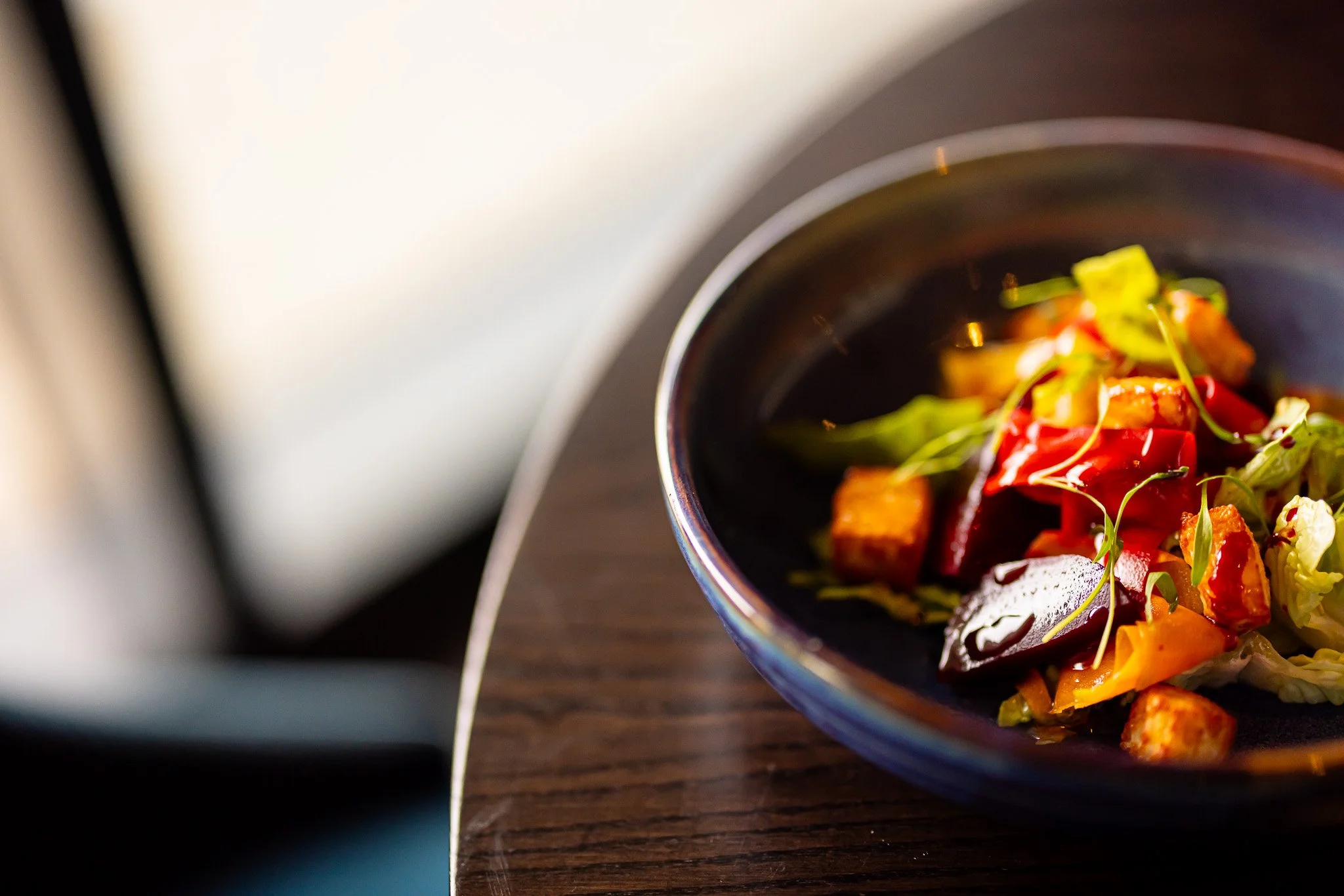 Colorful salad with mixed vegetables and greens in a black bowl on a wooden table.