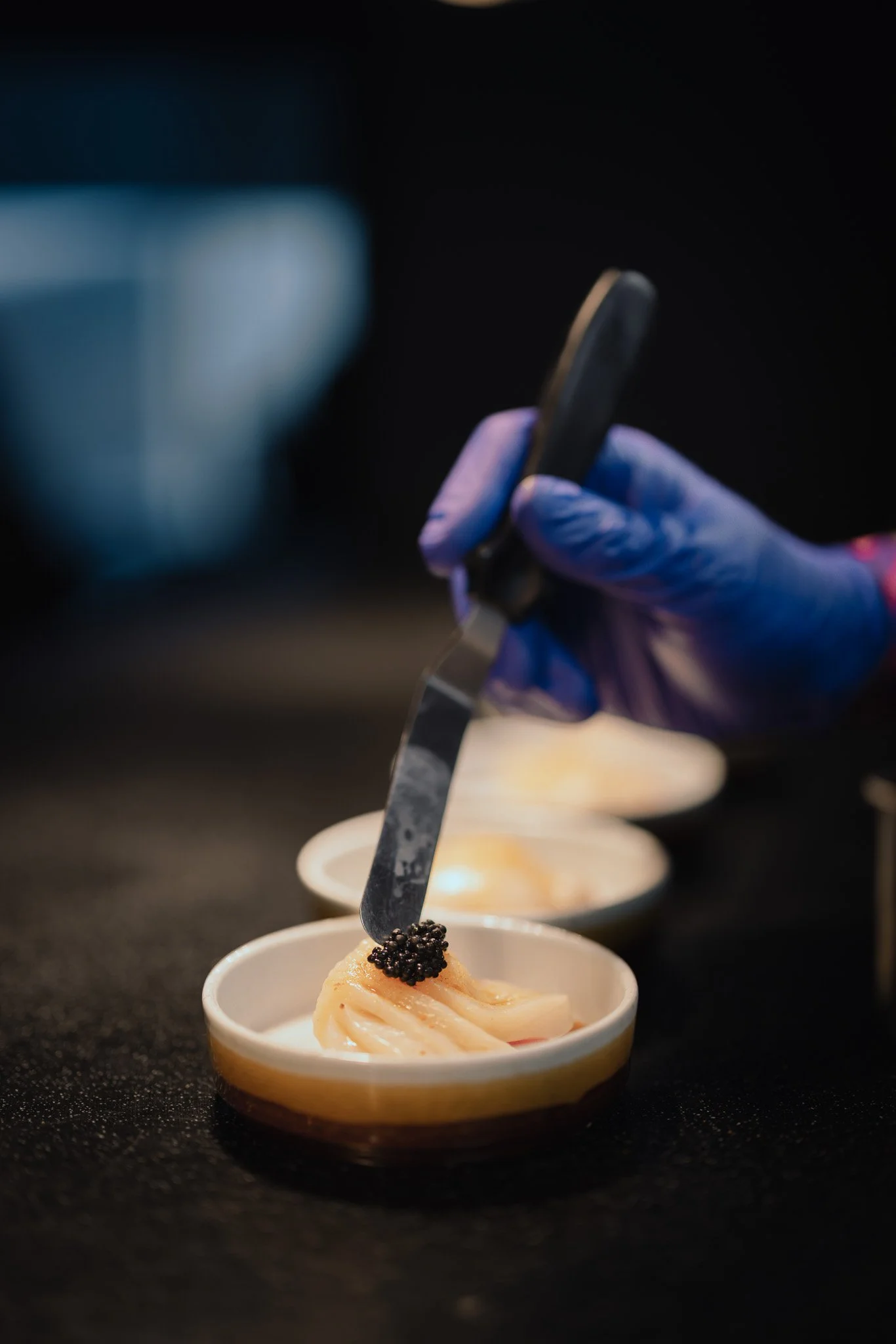 Chef placing black caviar on arranged slices of fish in small ceramic bowls.
