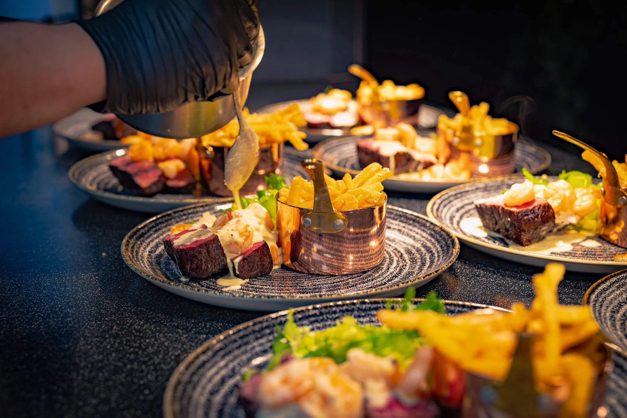 Chef preparing plated gourmet steak dishes with fries and vegetables in a professional kitchen.