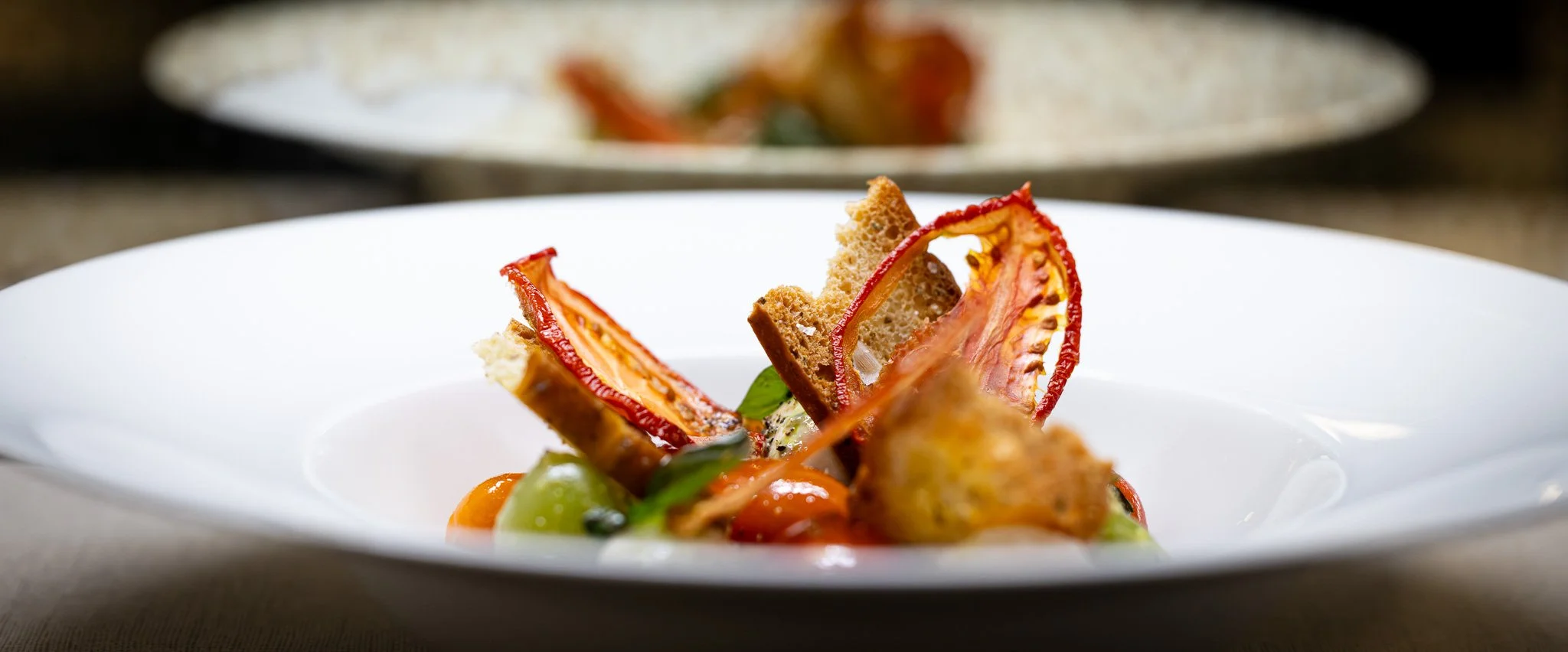 A plated gourmet dish featuring grilled vegetables, toasted bread, and fresh herbs, decorated with red pepper slices on a white plate.