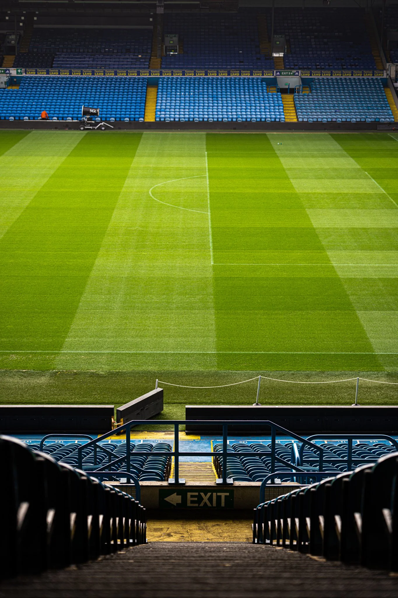 Empty soccer stadium view from the stands showing the field, seating areas, and exit sign.