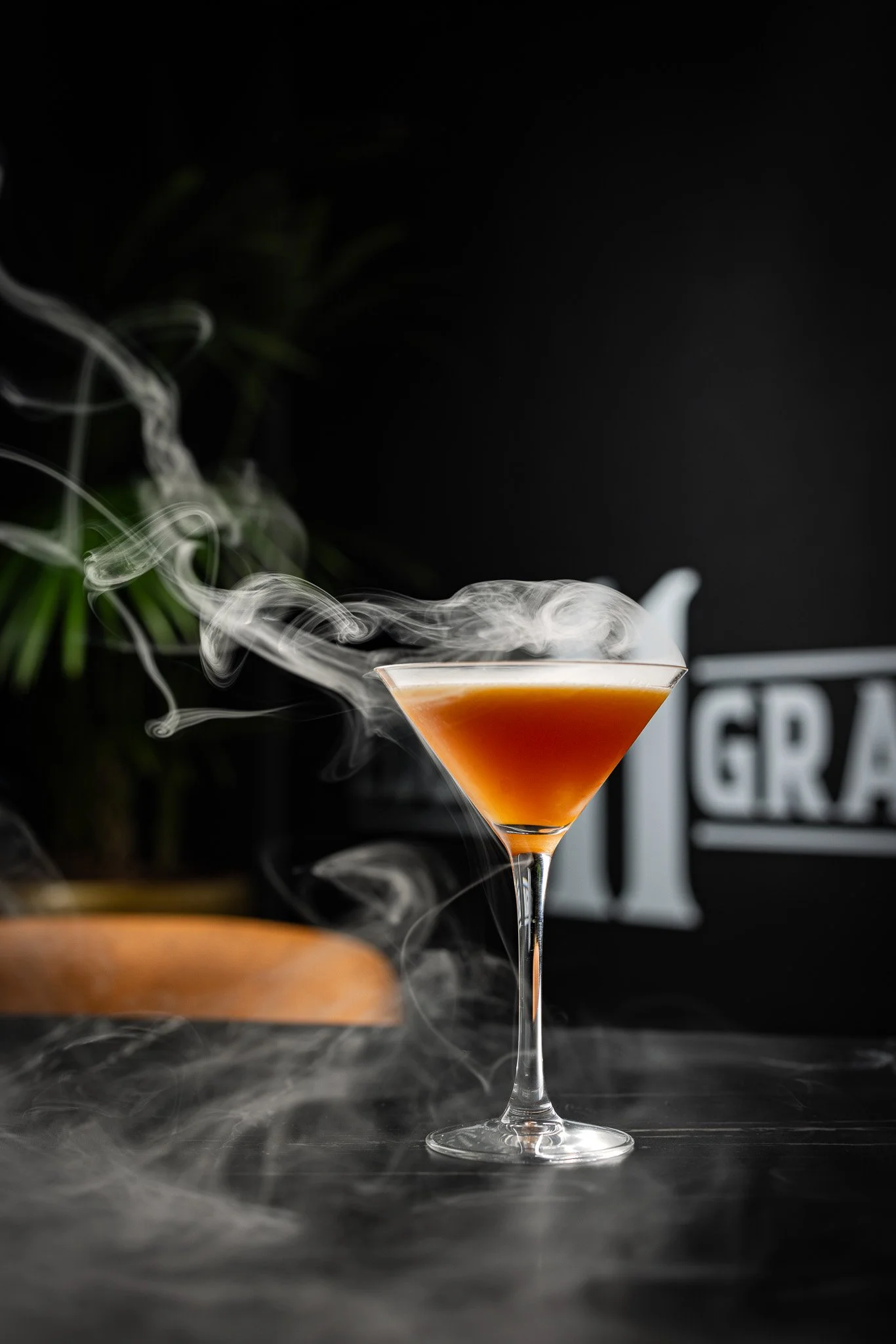 A cocktail with a smoky effect in a martini glass, with smoke swirling around and rising from the drink.