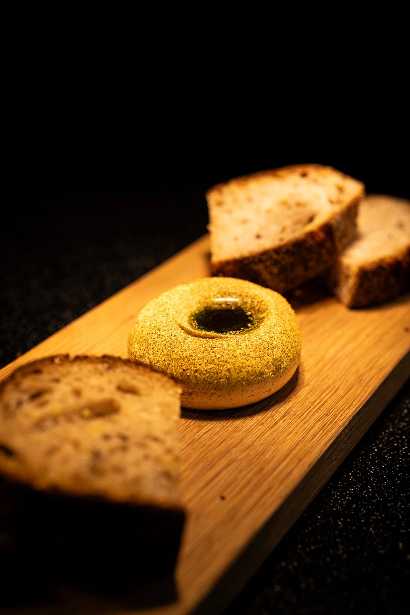 Appetizer of bread slices and a round cheese with herbs, served on a wooden board.