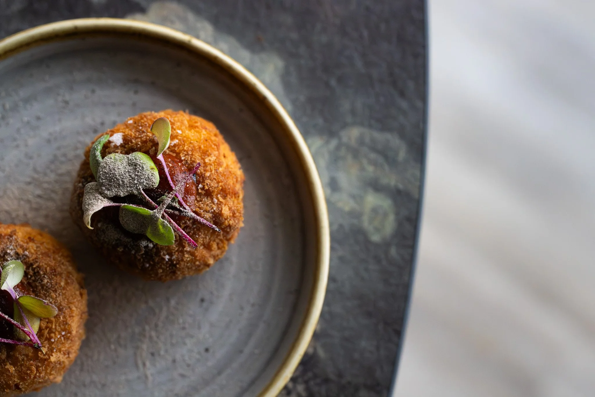 Two breaded fried balls garnished with microgreens on a ceramic plate.