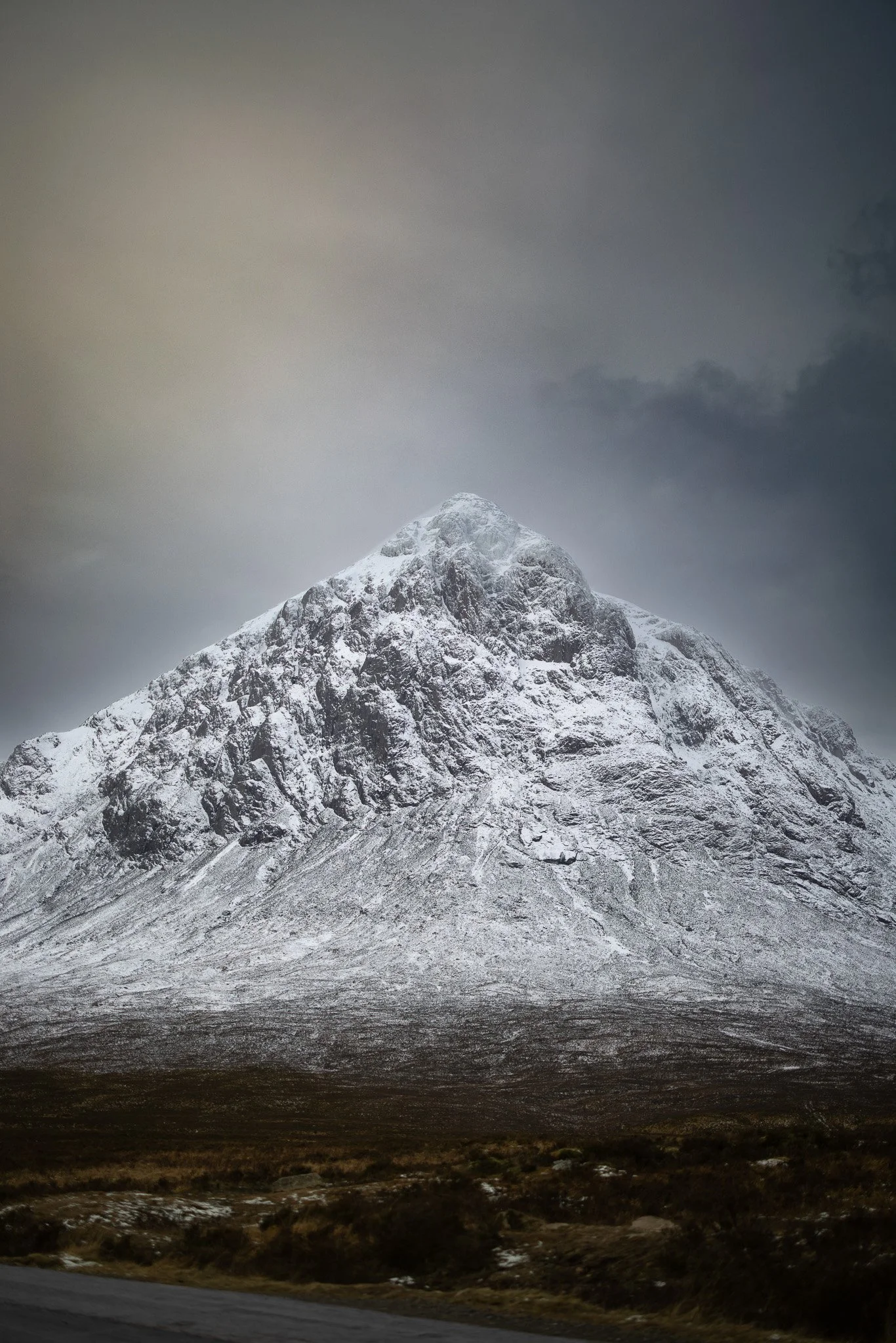 Snow-covered mountain under a cloudy sky, with a flat terrain at the base.