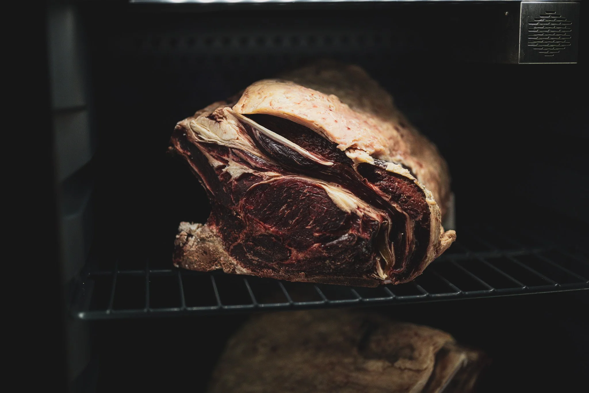 A large cut of raw beef resting on a metal rack inside an oven or dehydrator.