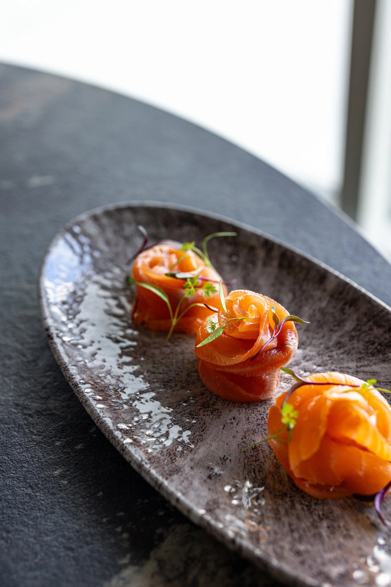 Three salmon tartare bites garnished with microgreens on a ceramic plate