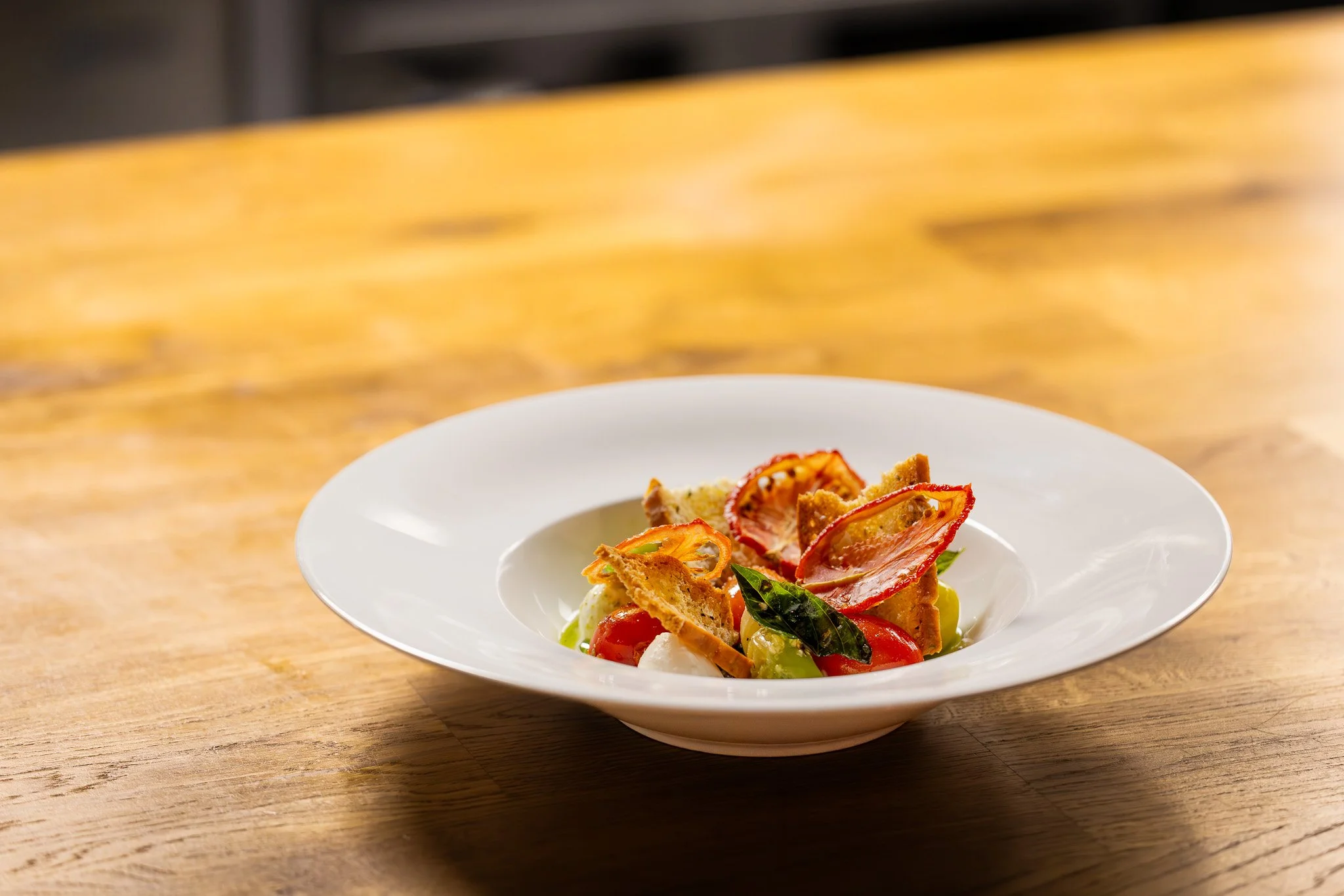 Chef's salad with tomatoes, bread croutons, lettuce, and basil on a white plate on a wooden table.