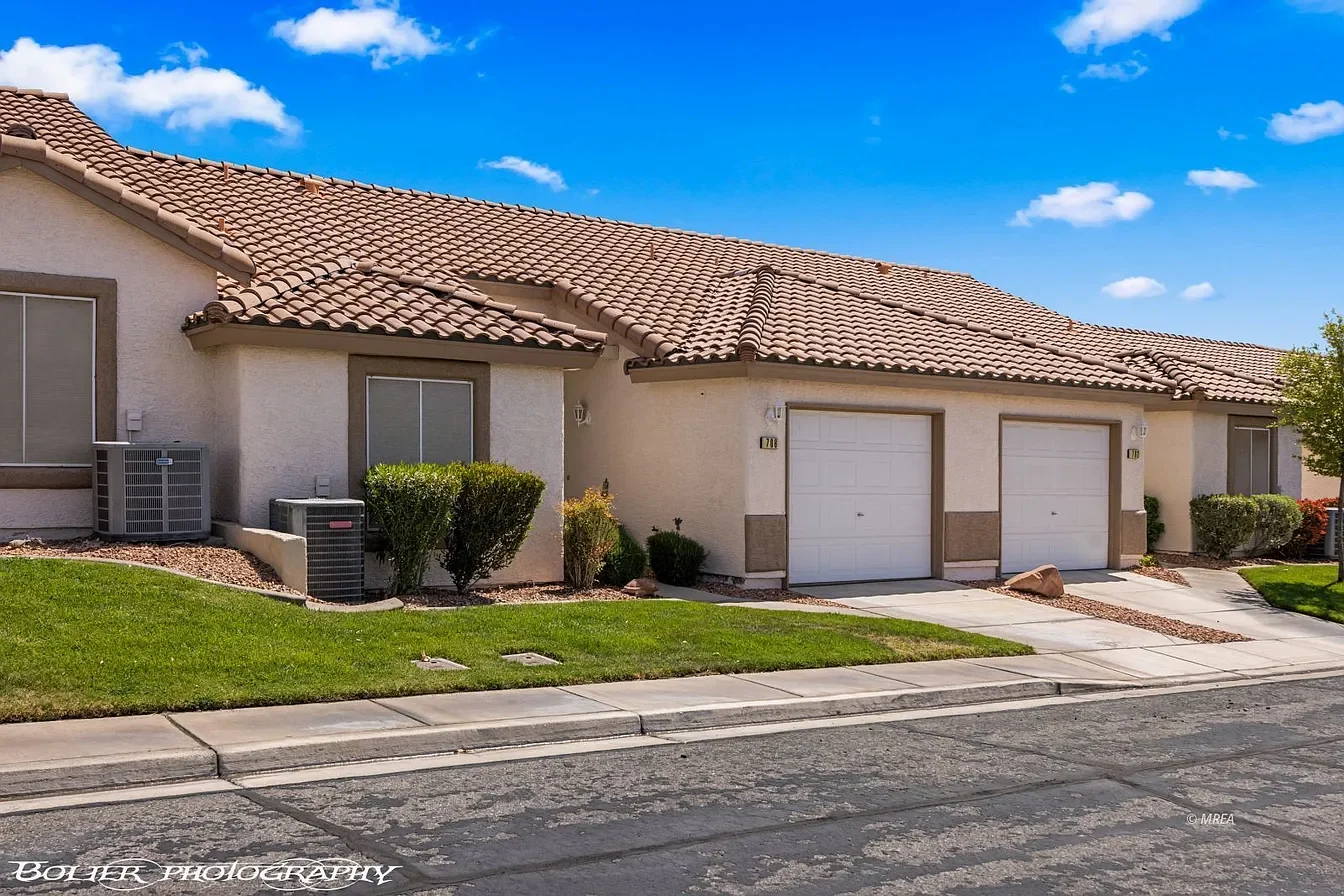 Featuring a stucco townhome with tile roof, attached garage, green landscaping, and desert-style architecture.
