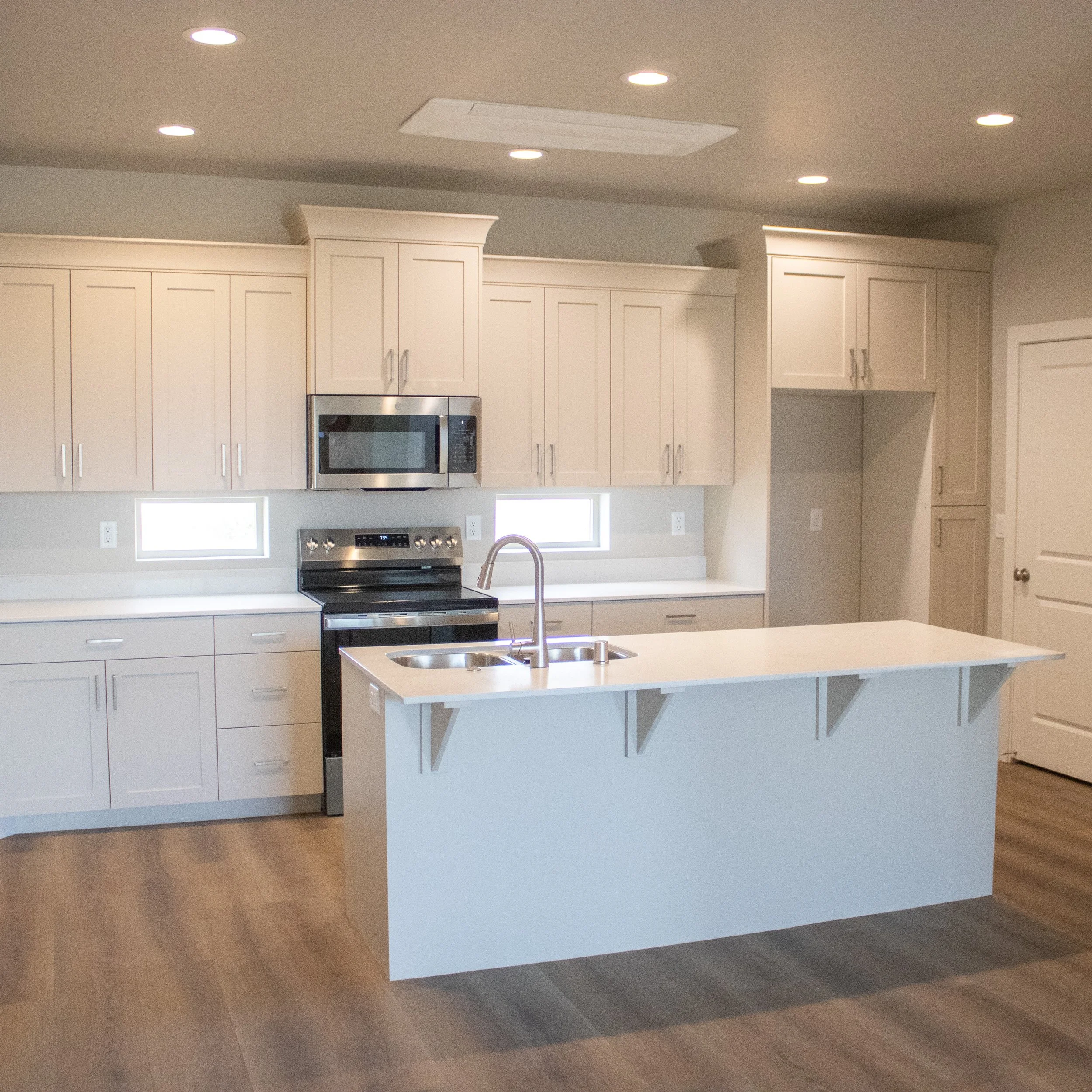 Bright, new construction kitchen featuring light beige shaker cabinets, a white quartz countertop on the island, and stainless steel appliances.