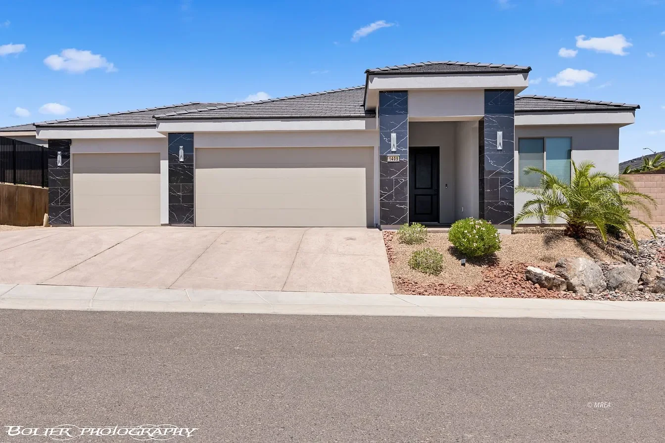 Modern luxury home exterior in Mesquite, Nevada featuring clean contemporary architecture, desert landscaping, a spacious three-car garage, and a bright blue sky backdrop.