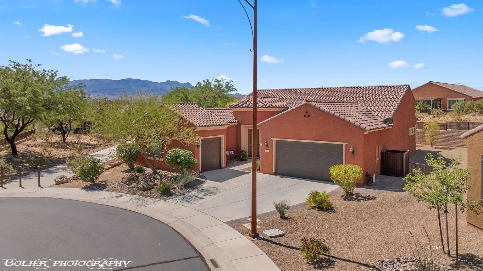 Beautiful single-story desert home on a spacious corner lot in Sun City Mesquite with mountain views, desert landscaping, and a three-car garage under a bright blue sky.