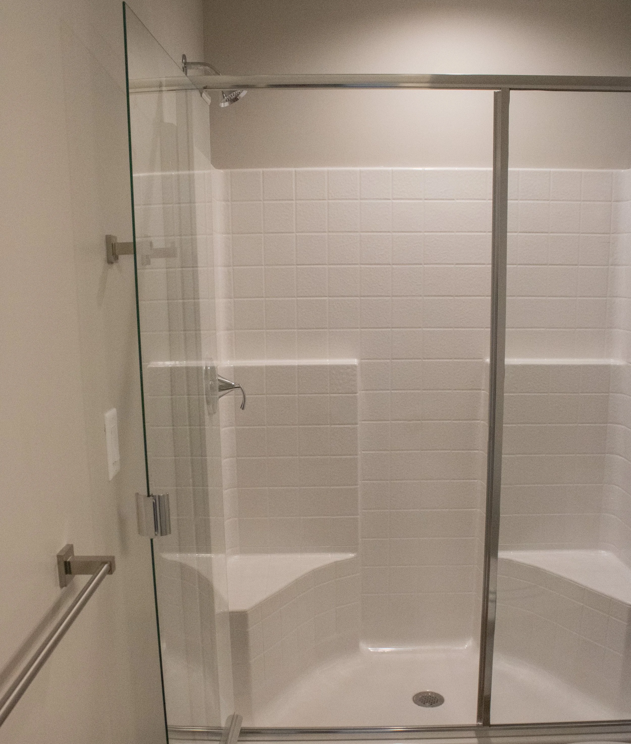 A modern walk-in shower with clear glass enclosure and light-colored tiled walls, featuring a built-in bench and a silver showerhead.