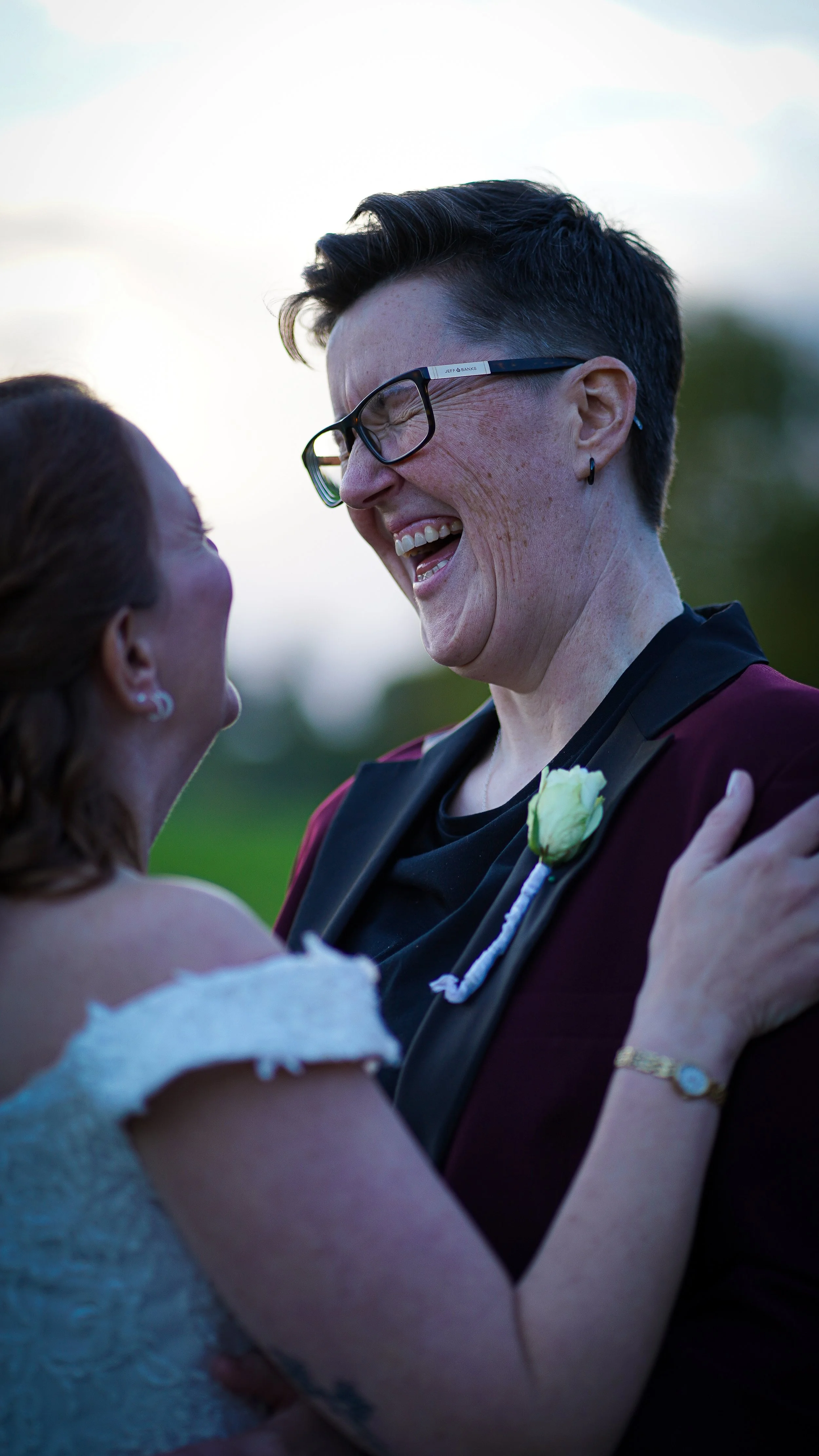 Two women sharing a joyful moment, embracing and smiling at each other outdoors during sunset.