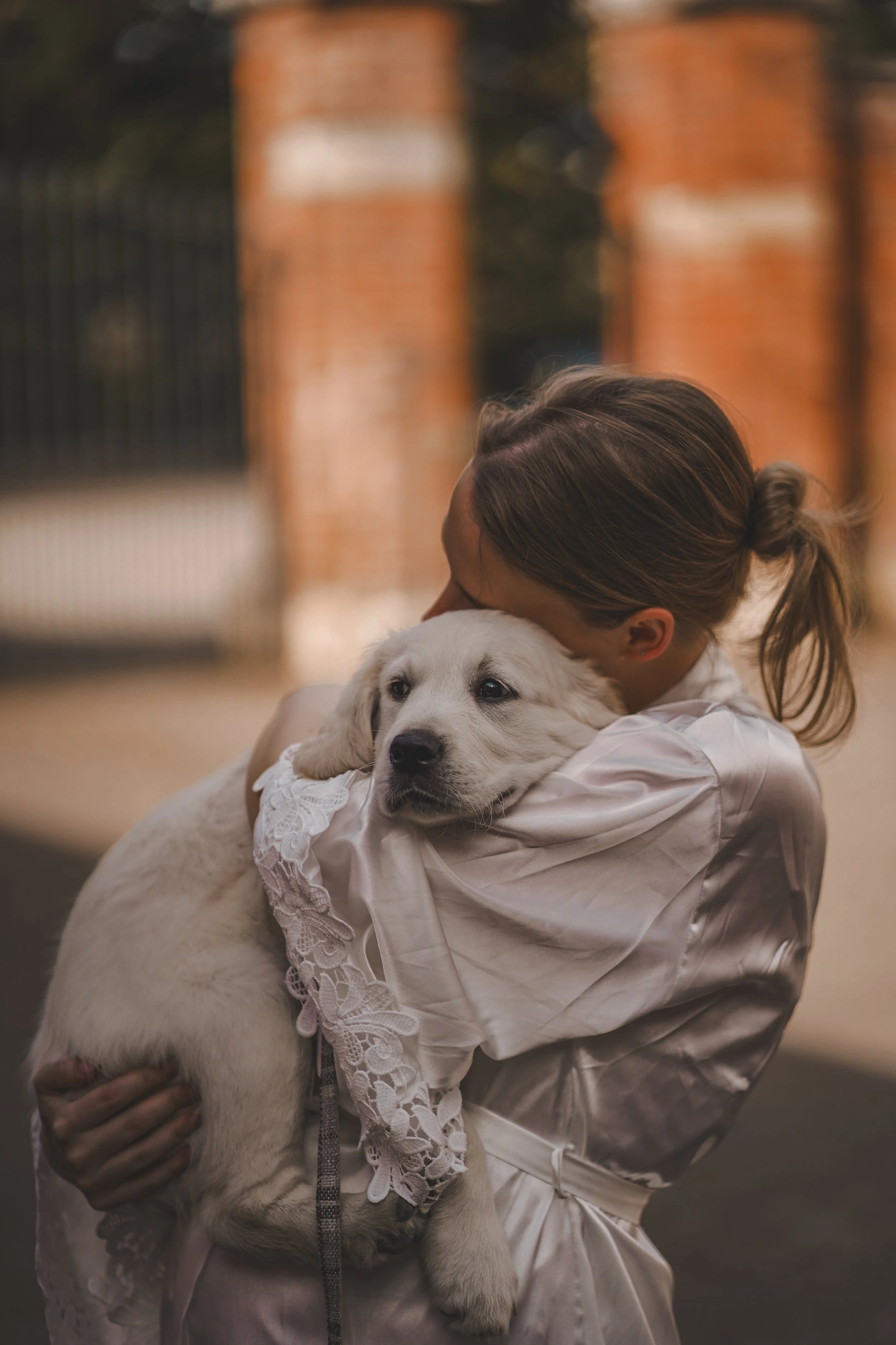 A woman hugging a white puppy with a black nose and blue eyes outside.