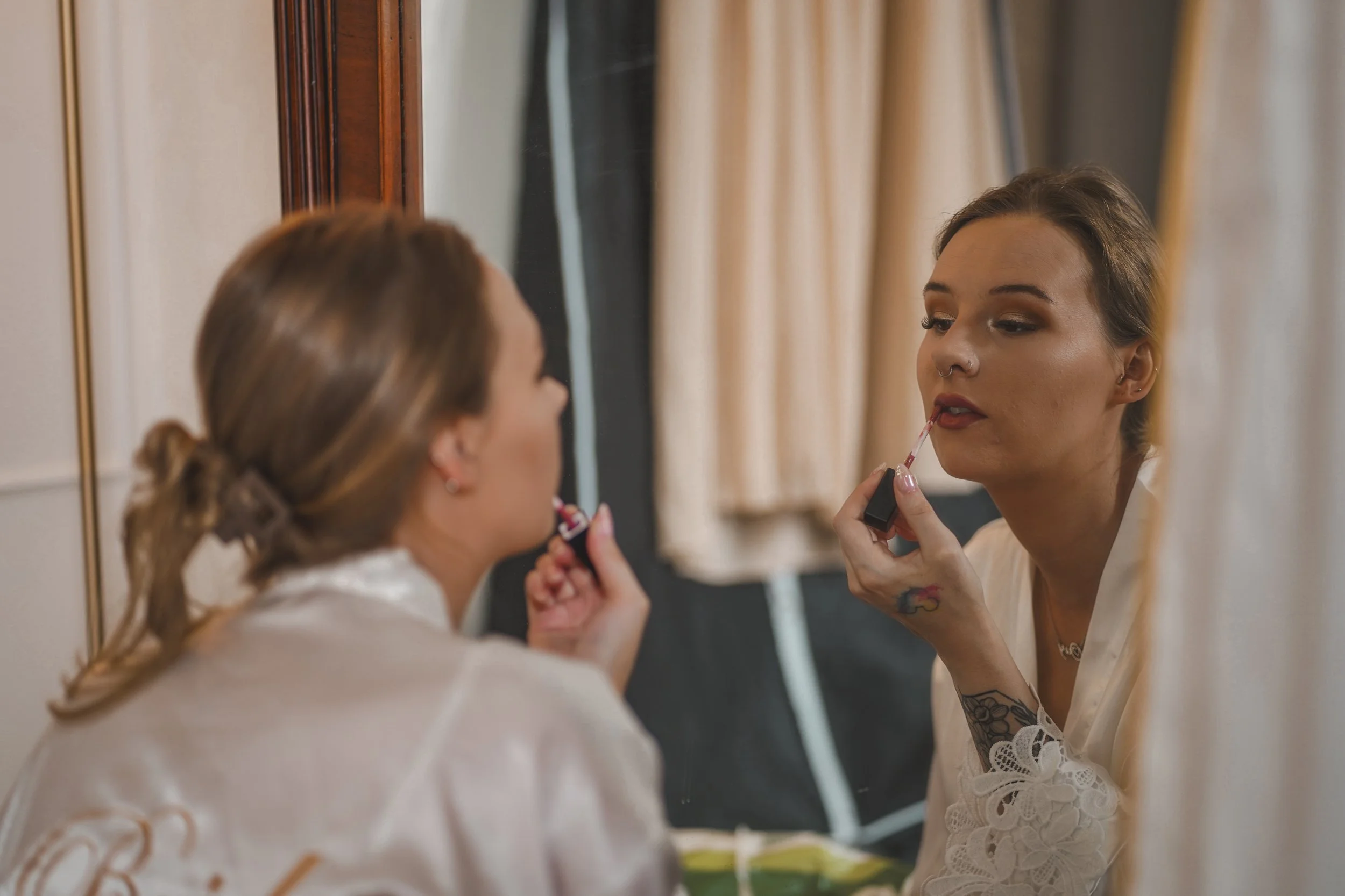Woman applying lipstick in front of mirror while looking at her reflection.