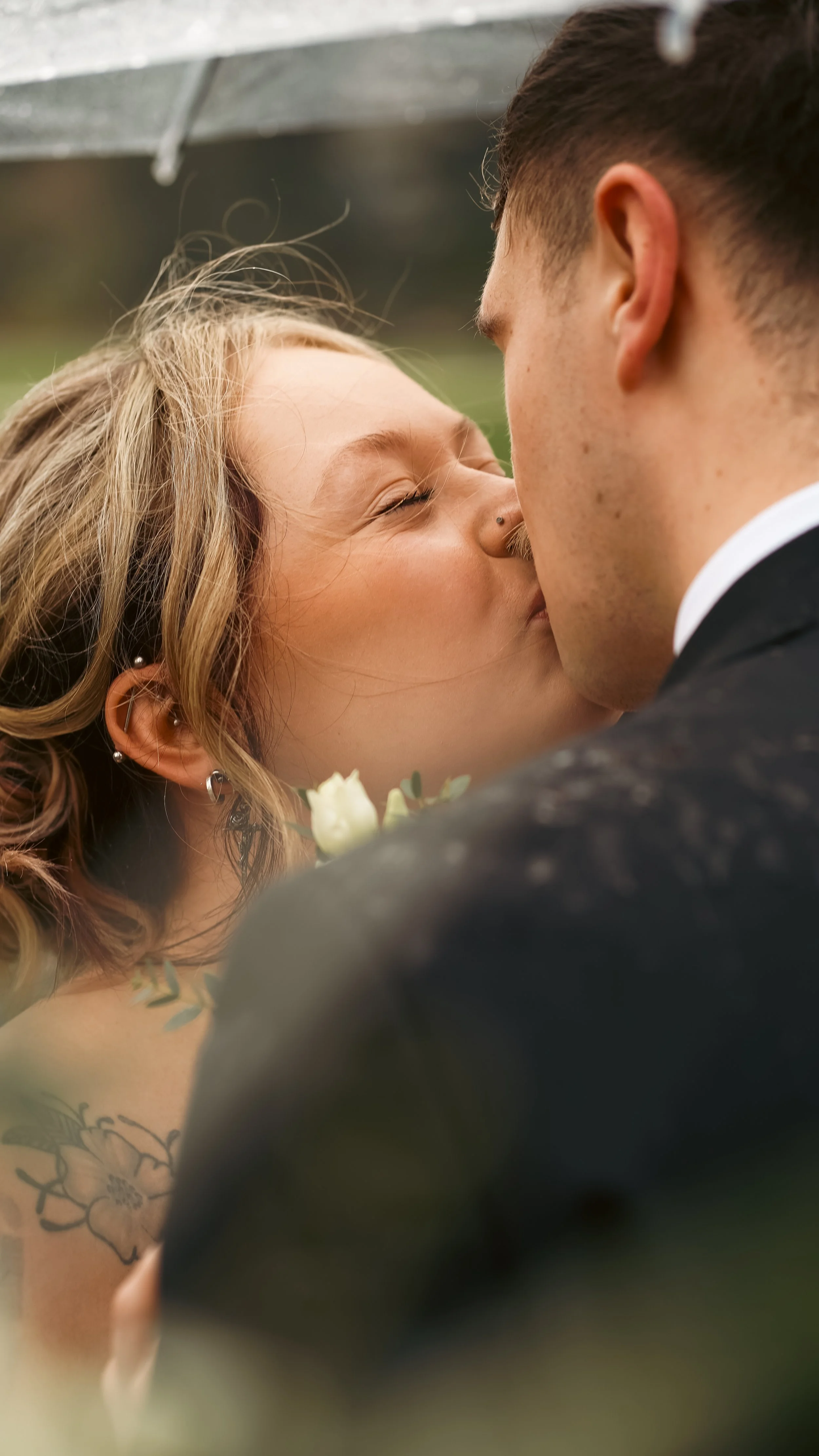 Close-up of a bride and groom sharing a kiss during their wedding outdoors, with the bride smiling and eyes closed.