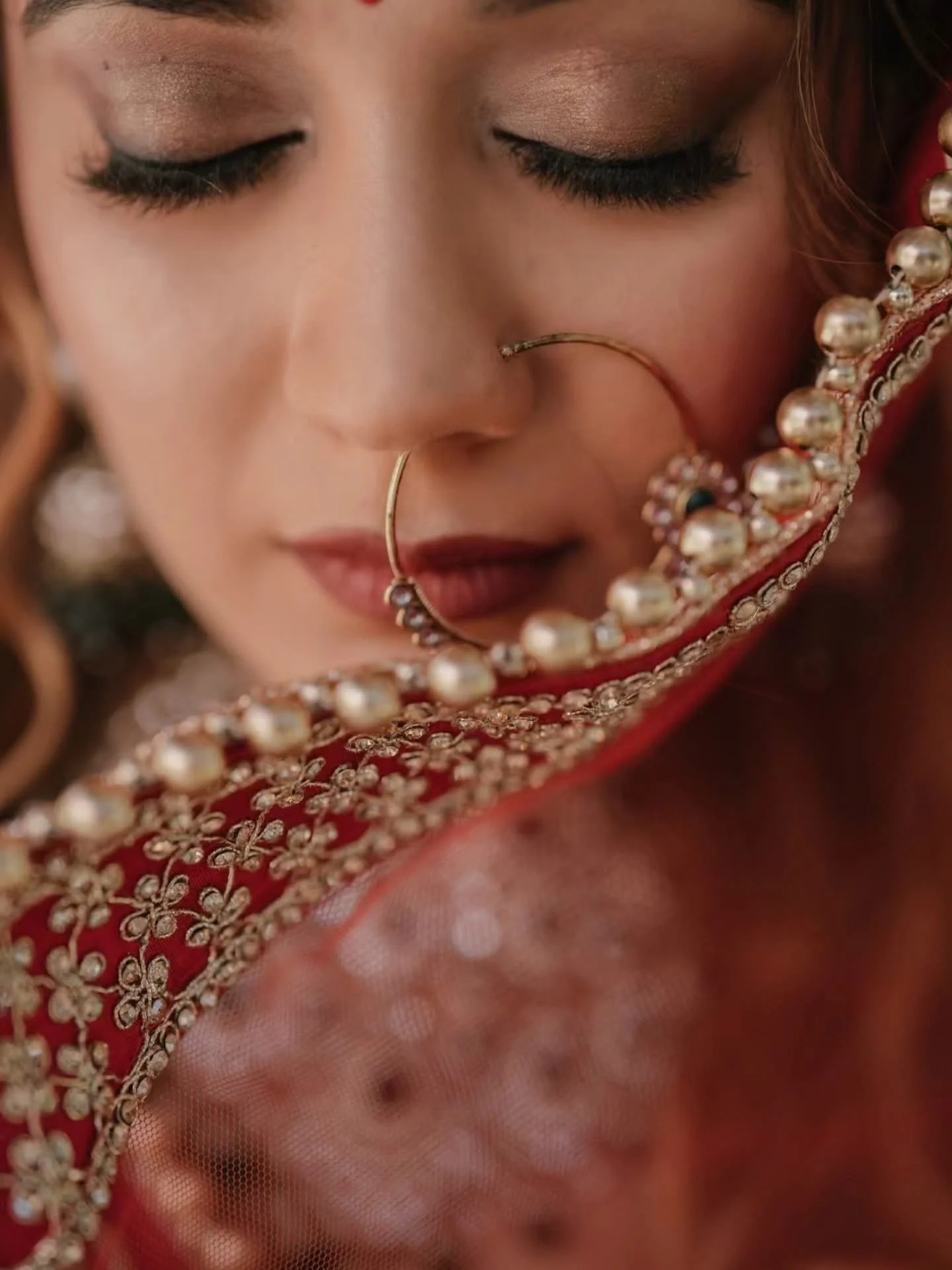 Close-up of a woman with closed eyes wearing traditional jewelry and red embroidered clothing.