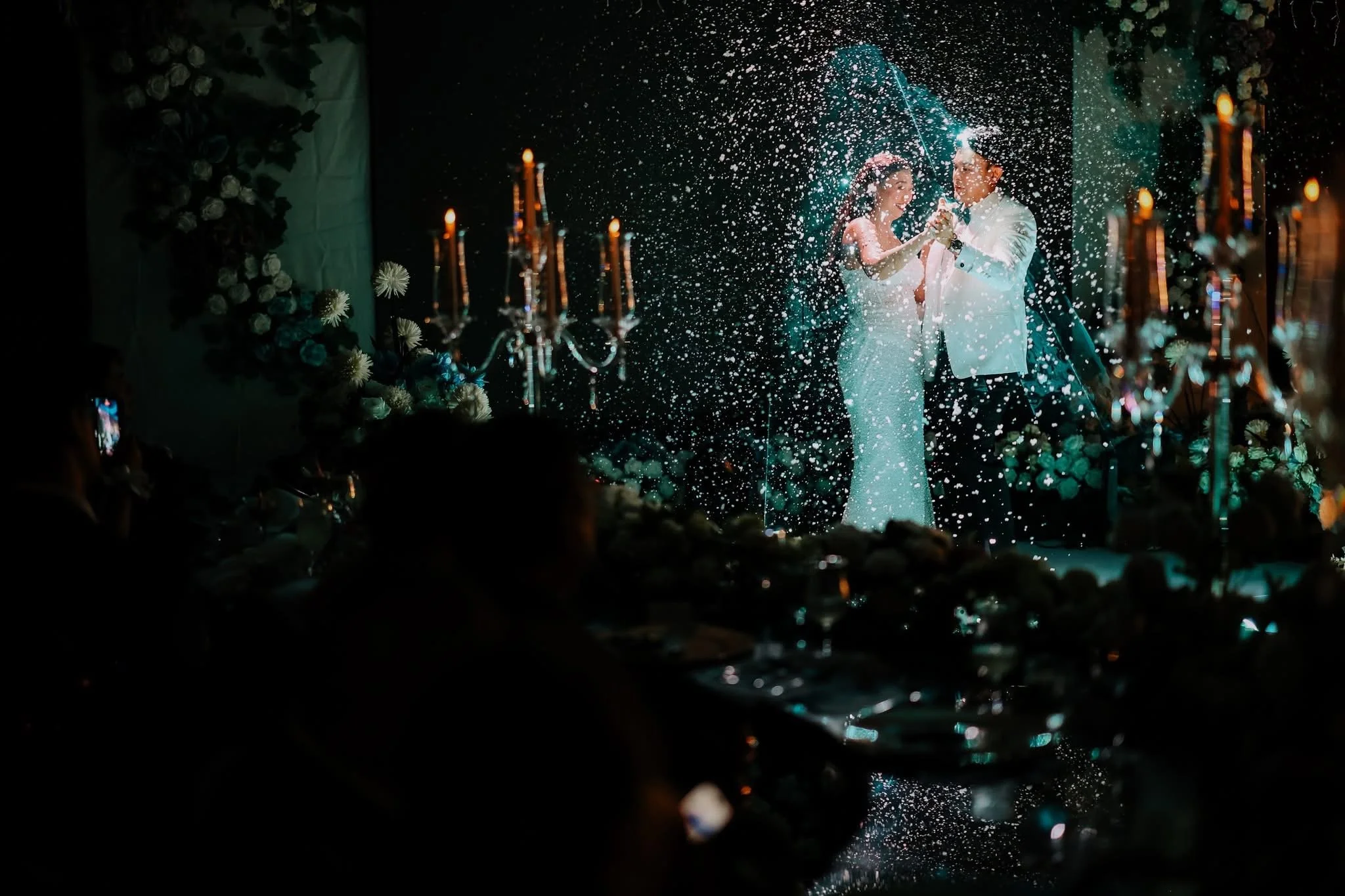 A couple dressed in wedding attire dancing under a shower of confetti at their wedding reception.