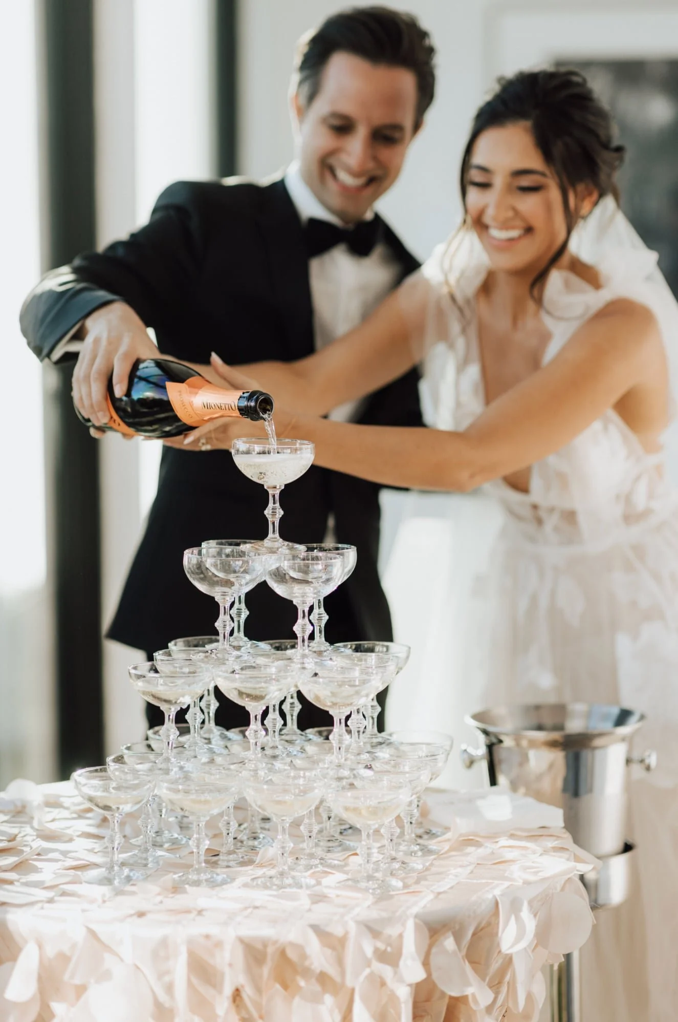 A wedding celebration with a bride and groom pouring champagne into a pyramid of glasses.