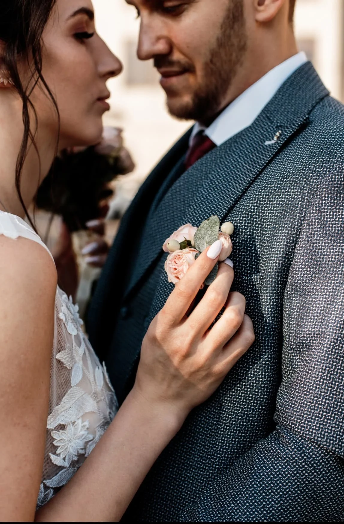 Close-up of a bride and groom in a romantic moment, with the bride pinning a pink flower boutonniere on the groom's suit jacket.