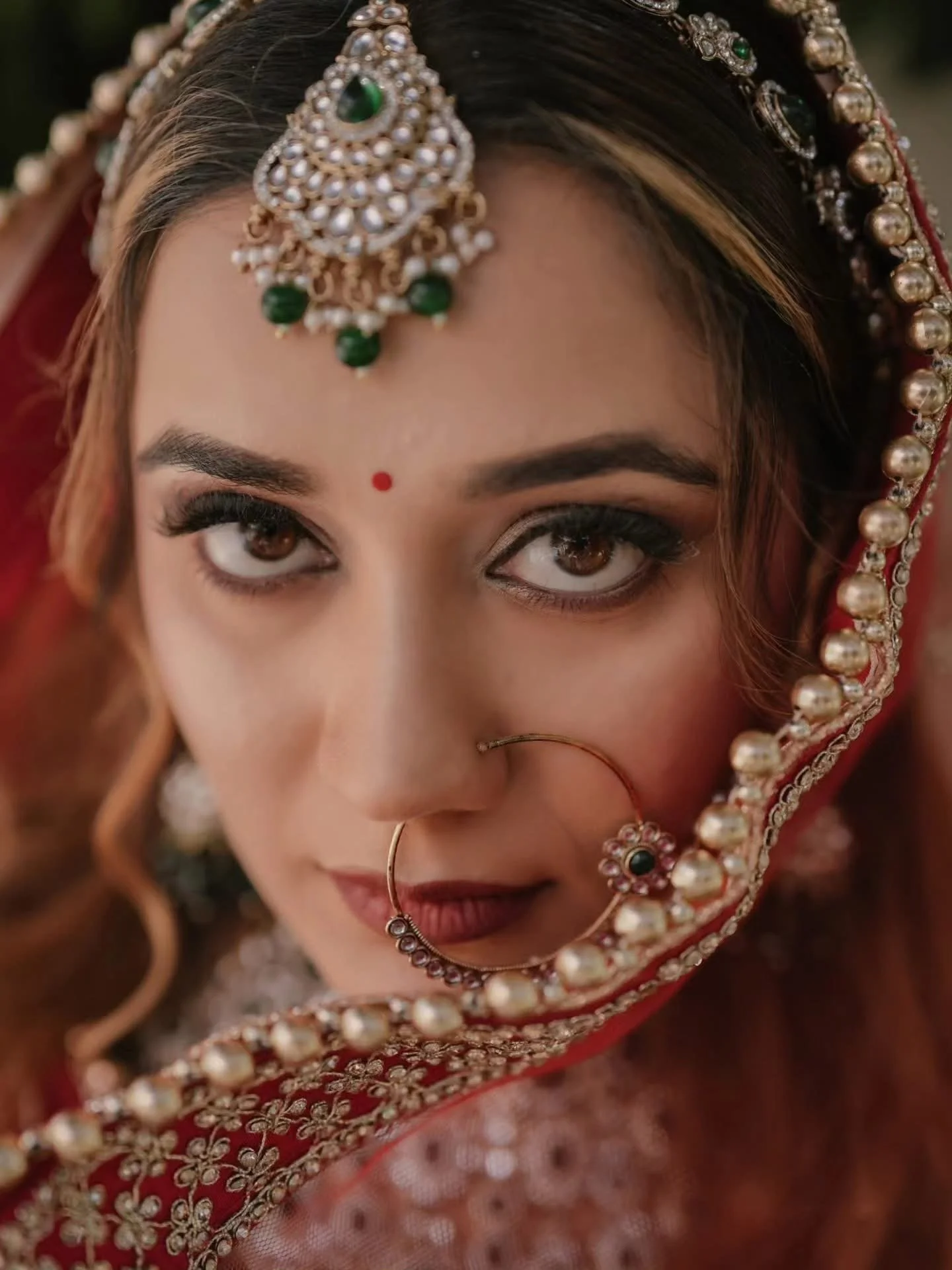 Close-up of a woman wearing traditional Indian jewelry and attire, with intricate headpiece and nose ring.