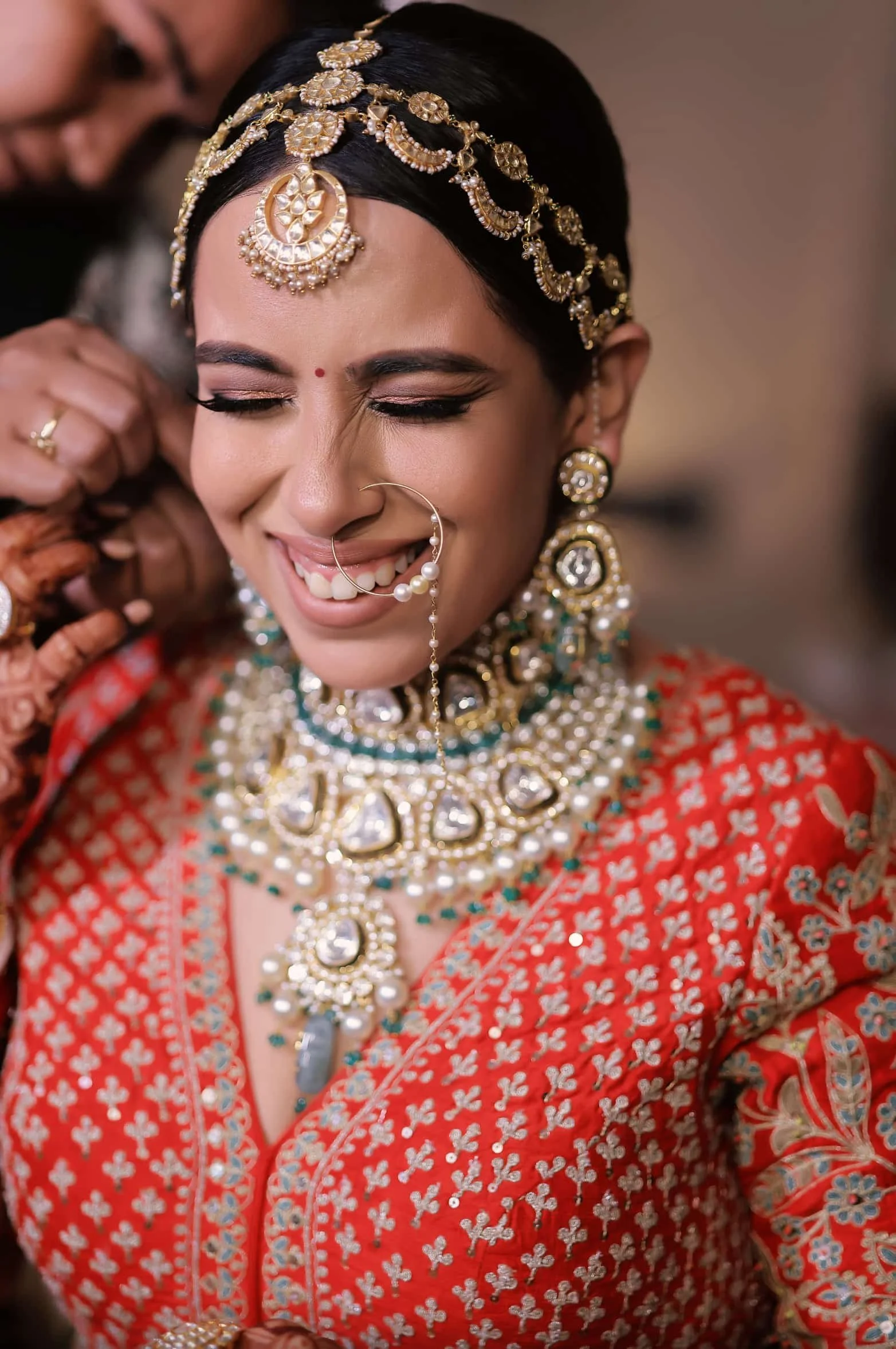 A woman dressed in traditional Indian attire, wearing elaborate gold jewelry including a headpiece, earrings, necklace, nose ring, and a red and gold embroidered sari.