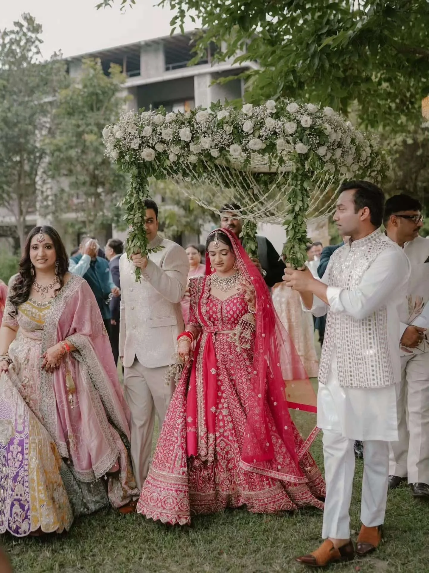 A group of people in traditional Indian attire participating in a wedding ceremony, holding a floral decorated canopy.