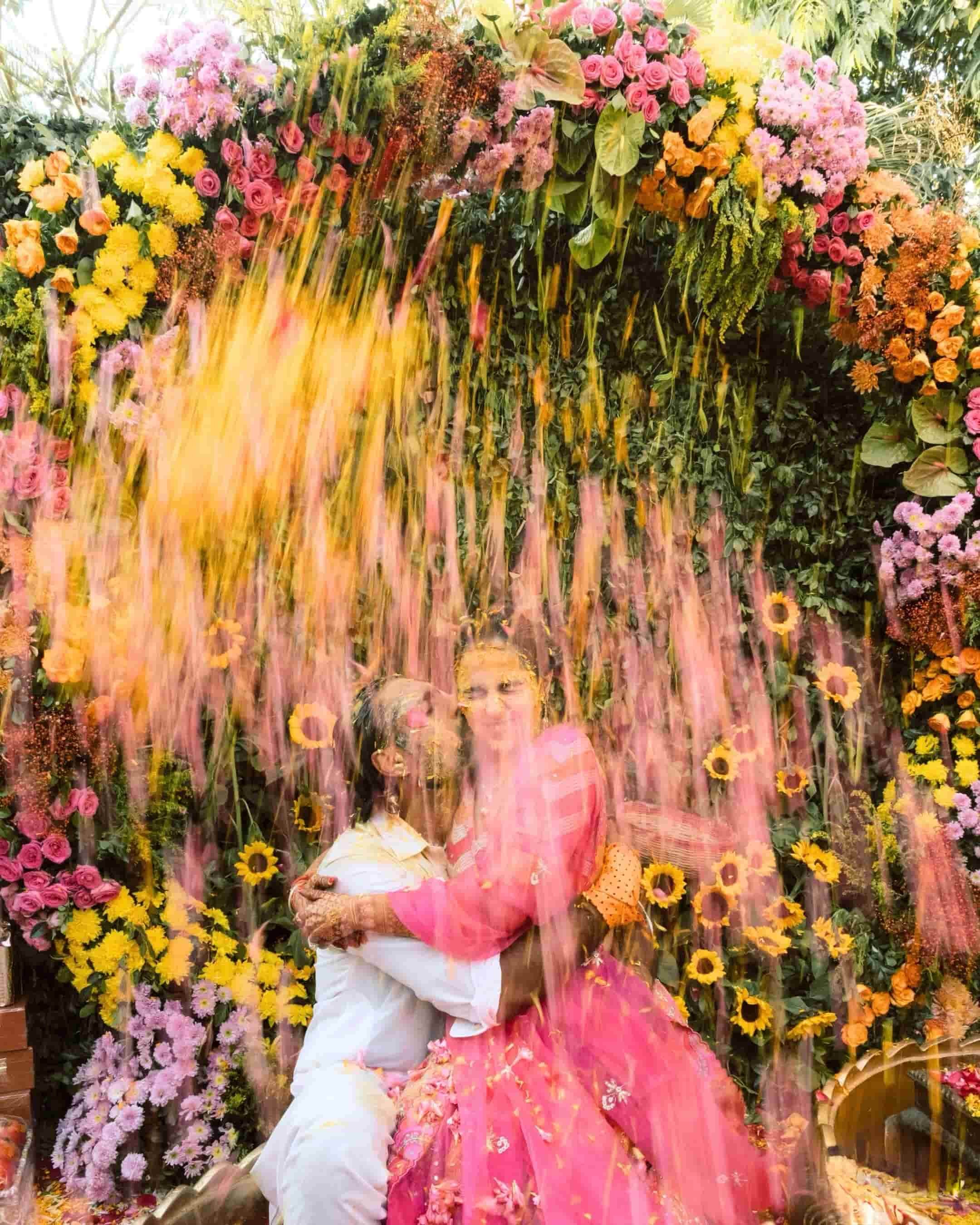 Two children at a colorful flower wall, with pink, yellow, orange, purple, and green flowers, some held or worn by the children.