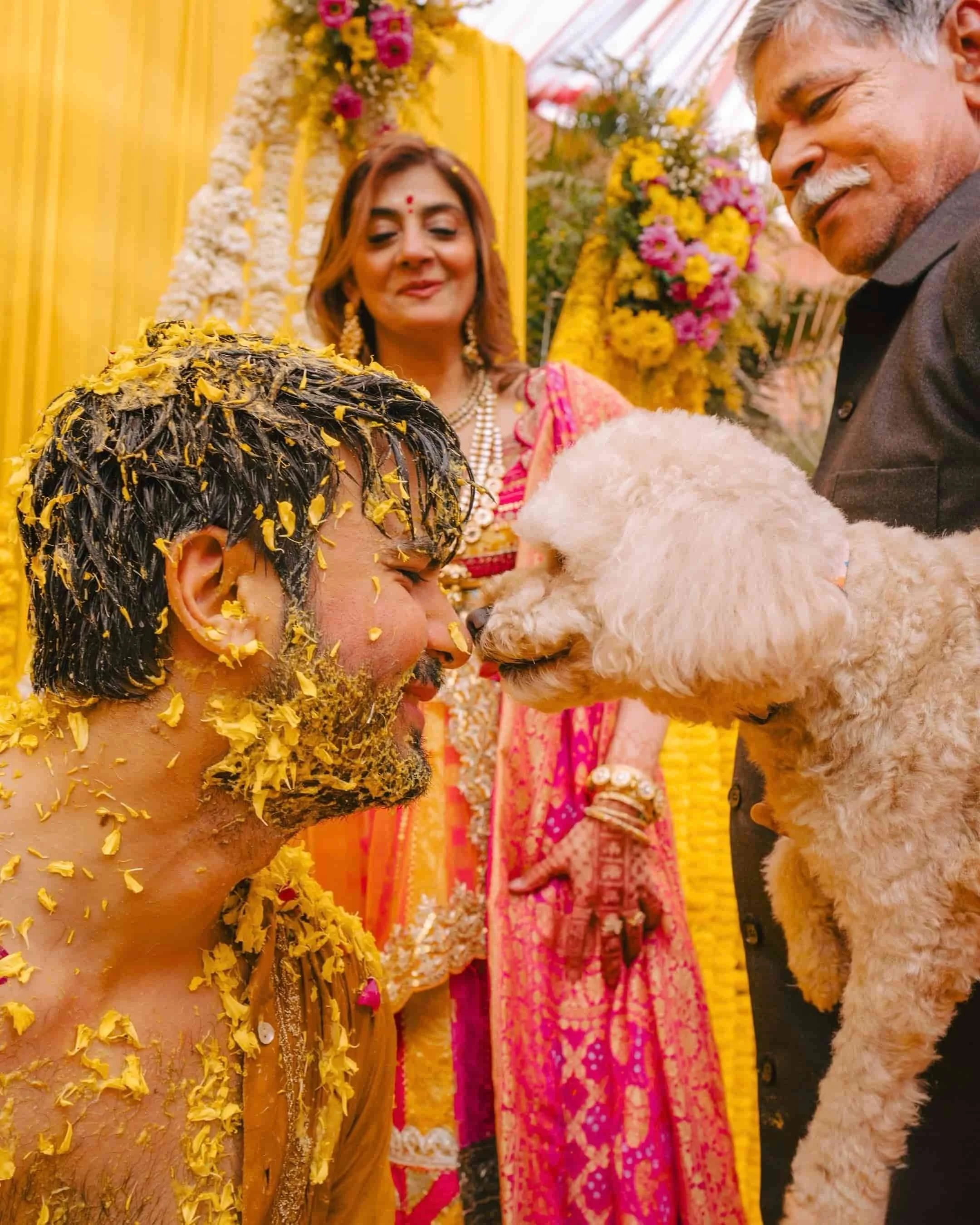 A couple, dressed in traditional Indian attire, participate in a wedding ceremony involving a sacred fire, surrounded by flowers and vibrant decorations.