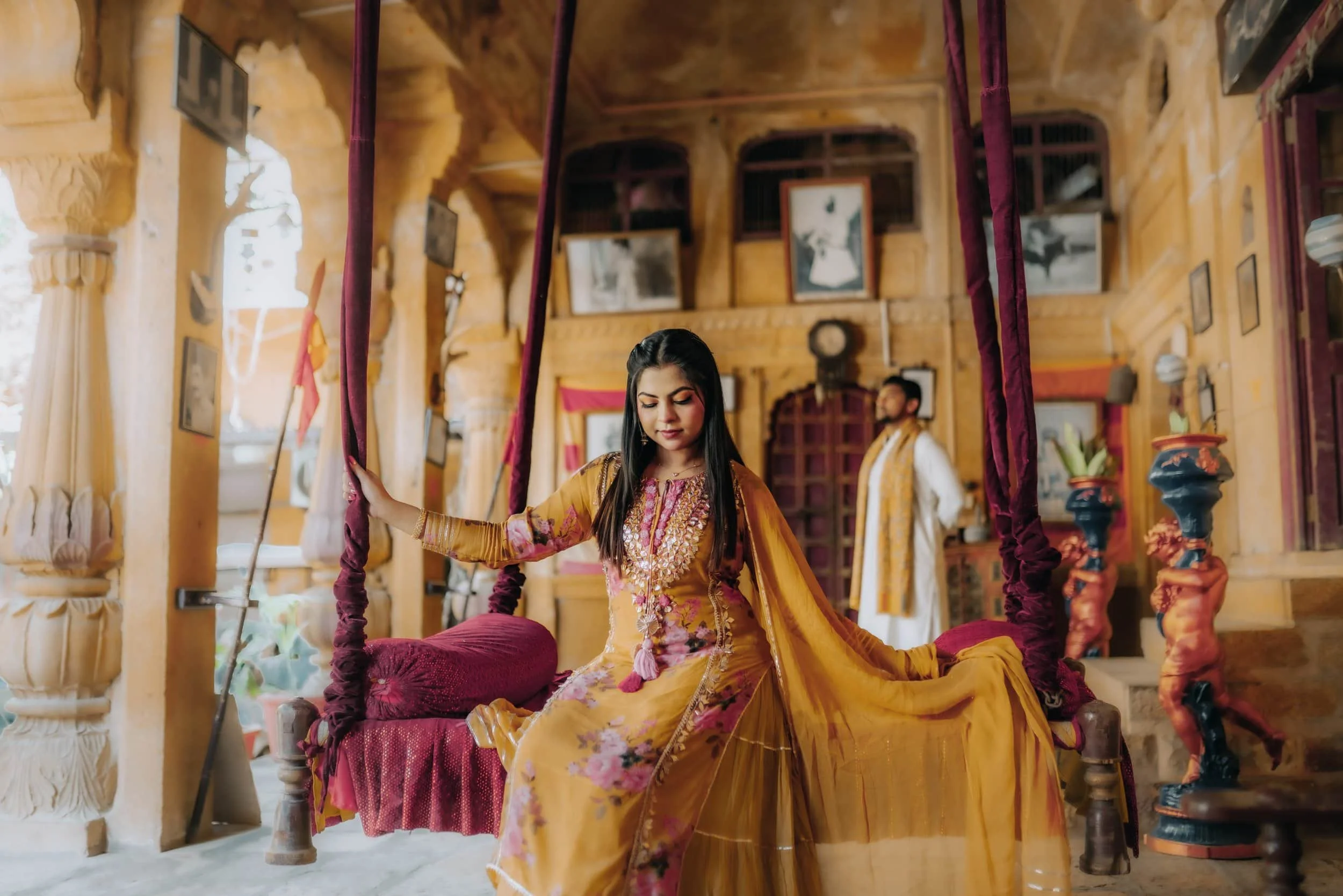 Young woman in traditional Indian attire on a swing inside a decorated room.
